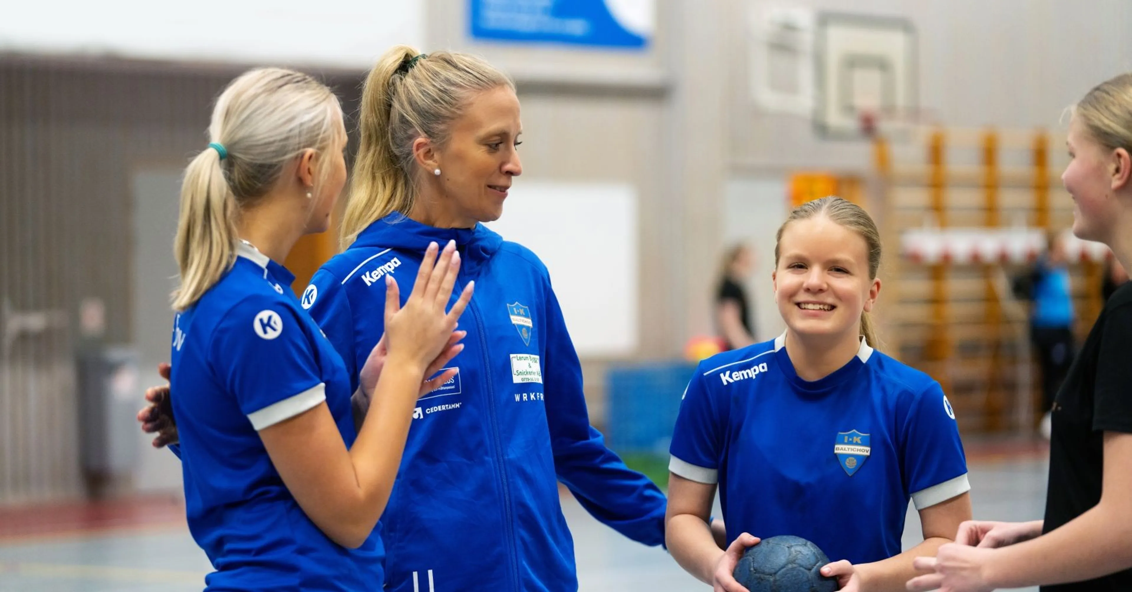 Tre tjejer i blåa handbollströjor på en handbollsplan