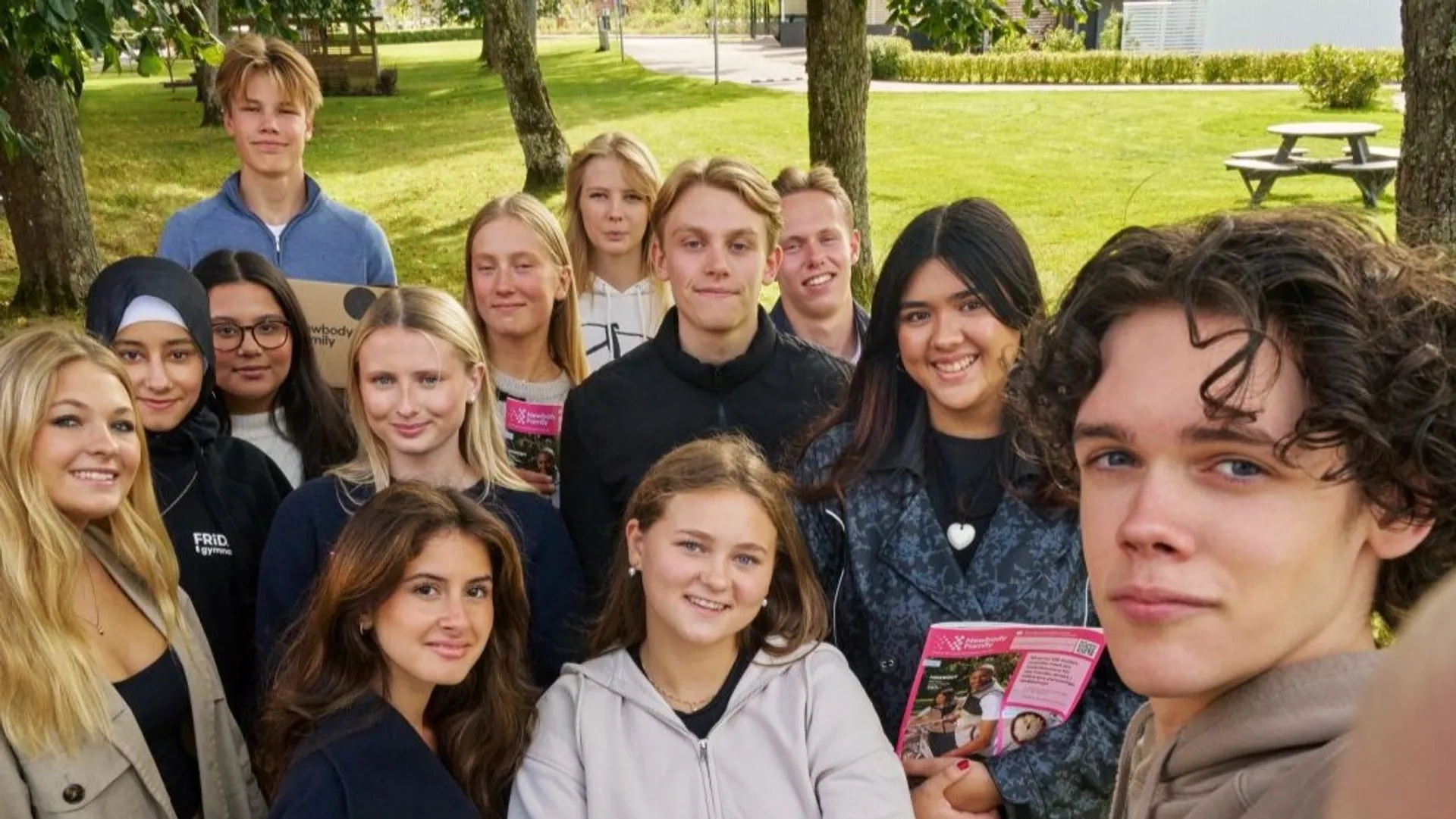 Gymnasieelever som står samlade på en gräsmatta och håller i newbody kataloger