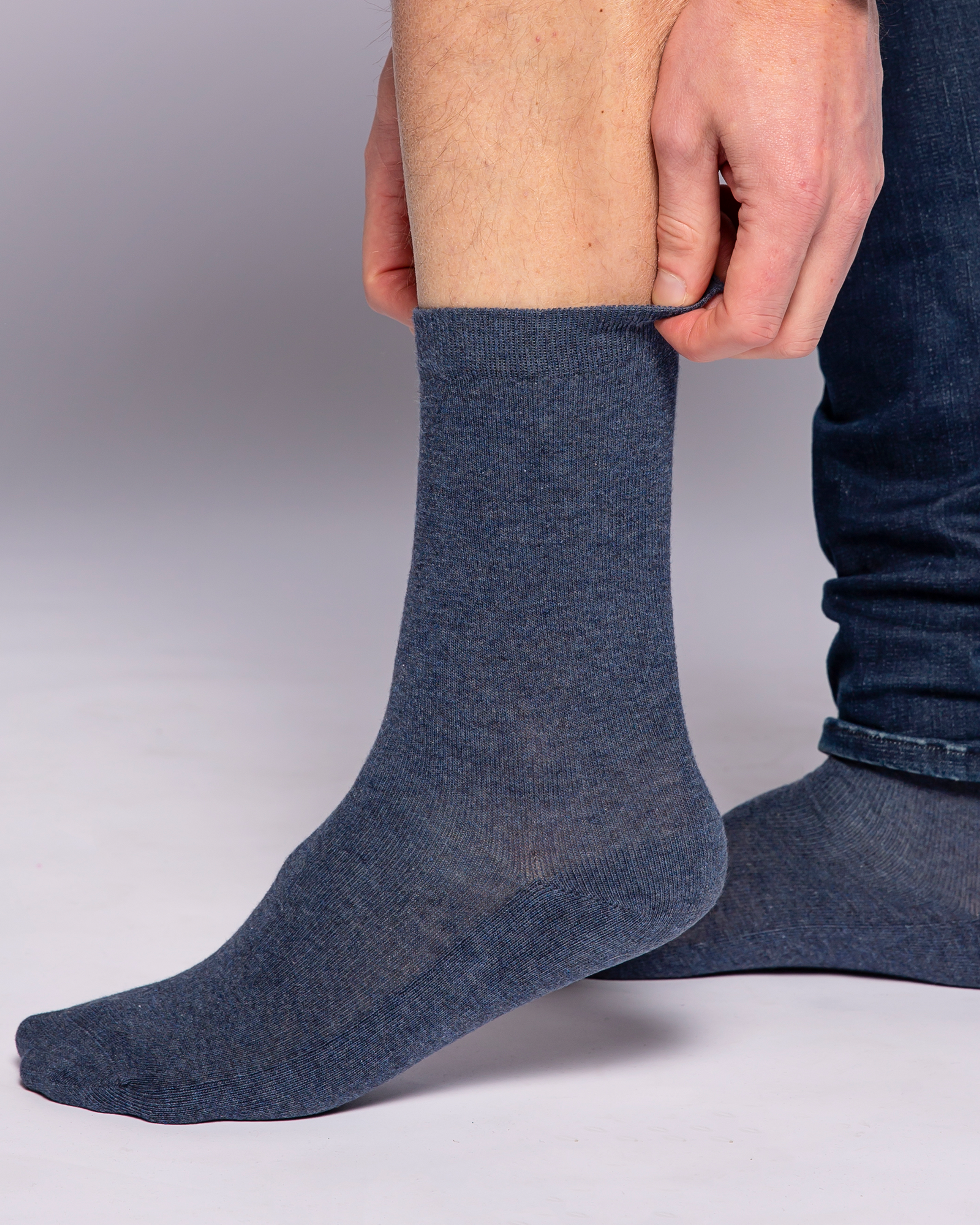 Mörkblå strumpor i mjukt, tunt material som sitter bekvämt runt ankeln. En hand justerar strumpans övre kant för en perfekt passform.