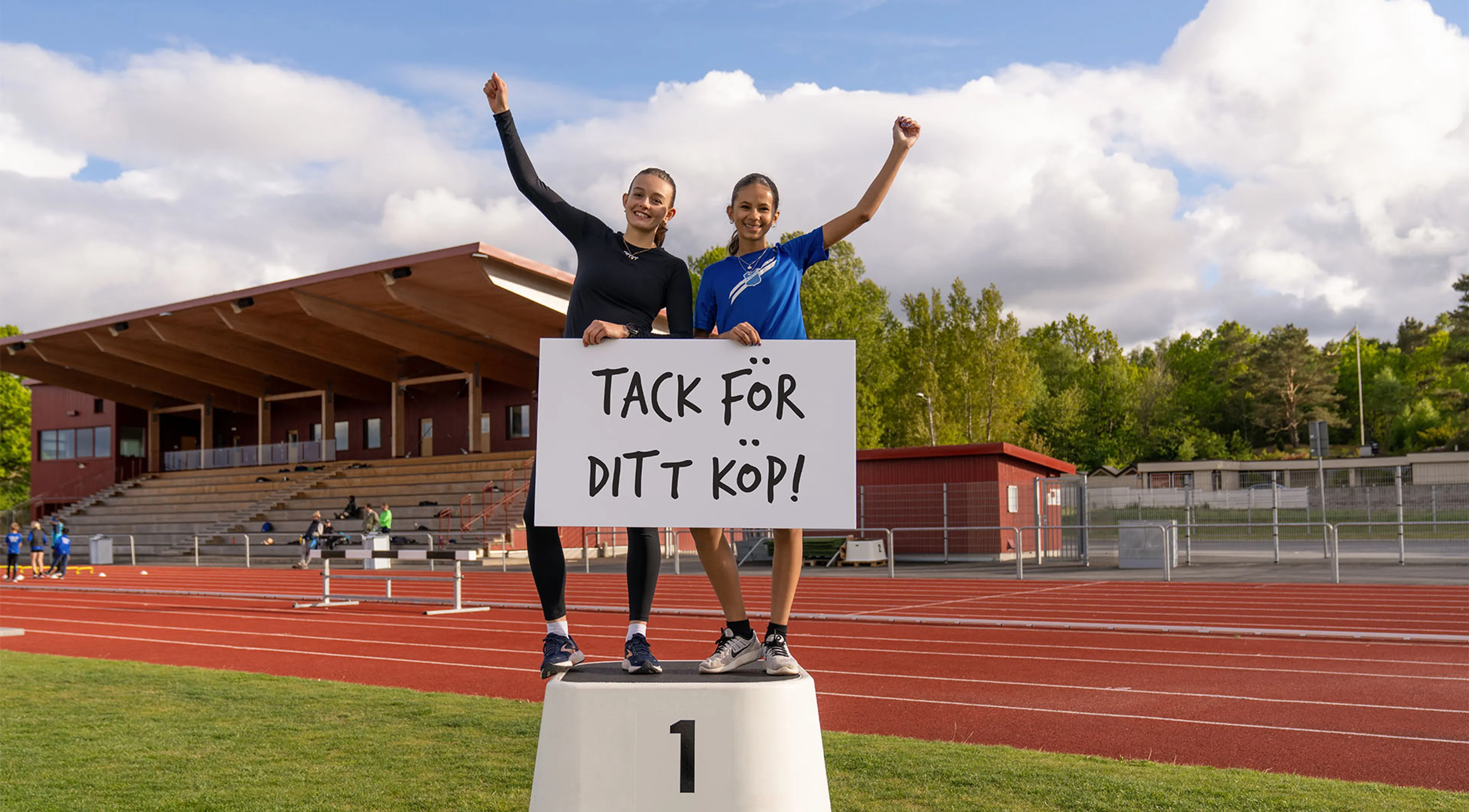 två tjejer på en prispall med en skylt i händerna där det står "Tack för ditt köp!"