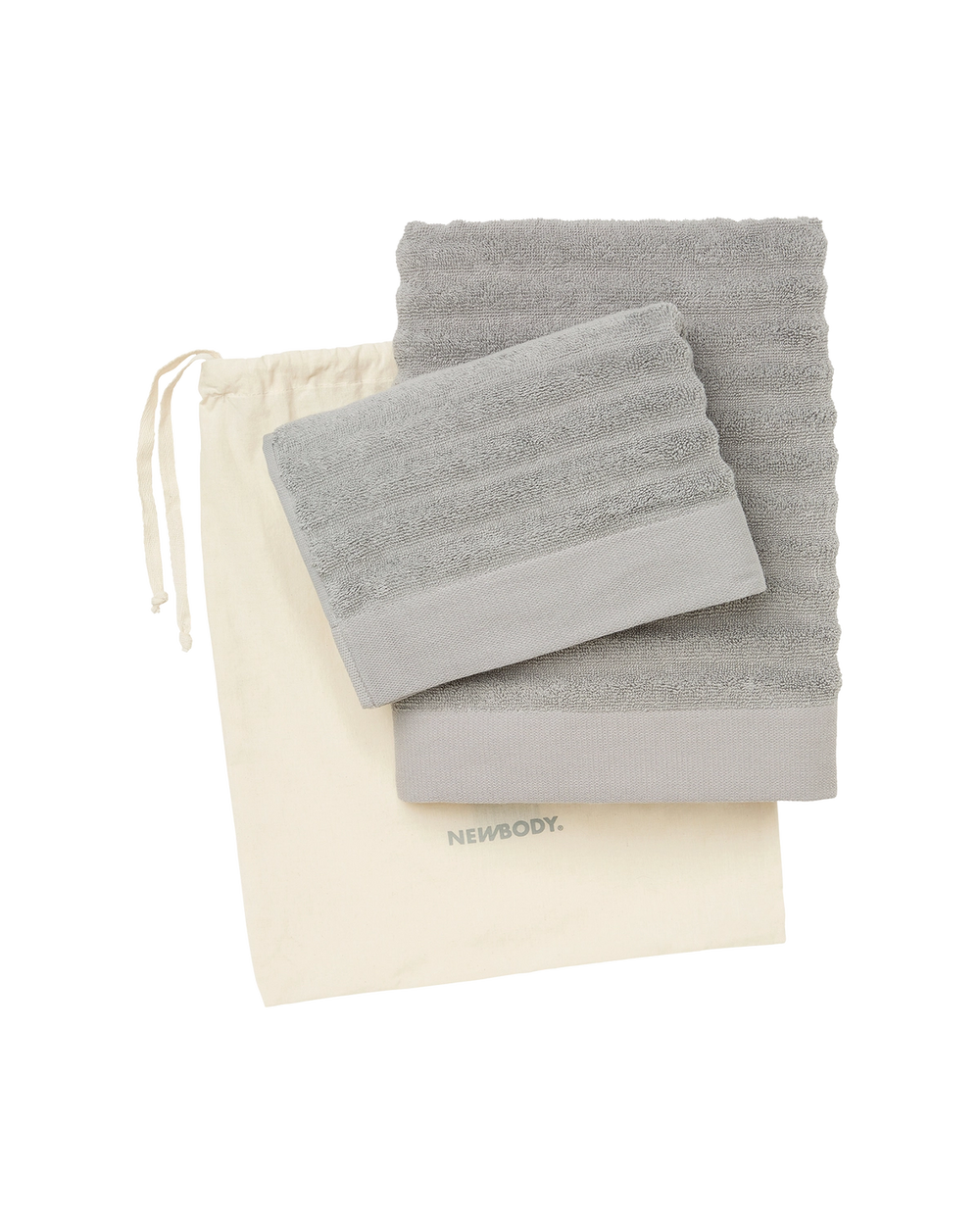 Två mjuka handdukar i olika grå nyanser, vikta ovanpå en naturfärgad påse med dragsko. Handdukarna har en diskret vågmönstrad struktur och enfärgad kant.
