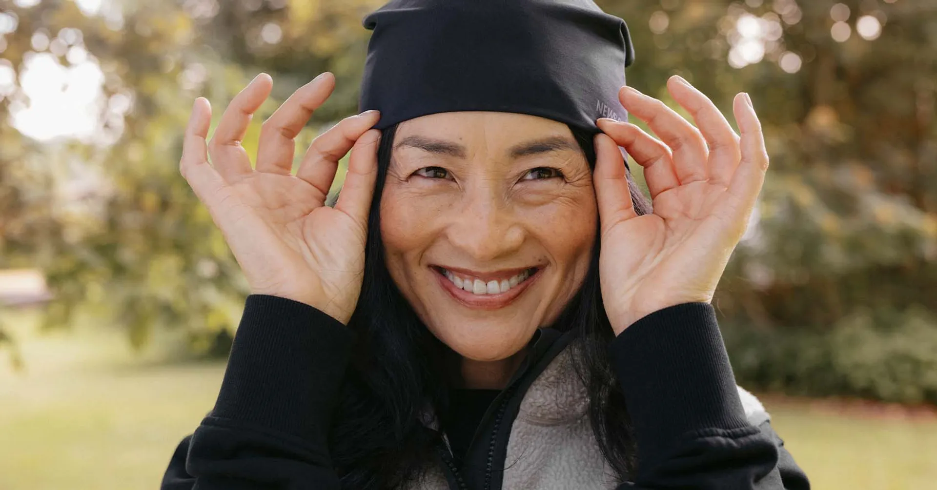 En varm mössa i mjukt material med en justerbar passform, här på en leende person utomhus. Mössan är svart och passande för kyligare dagar.