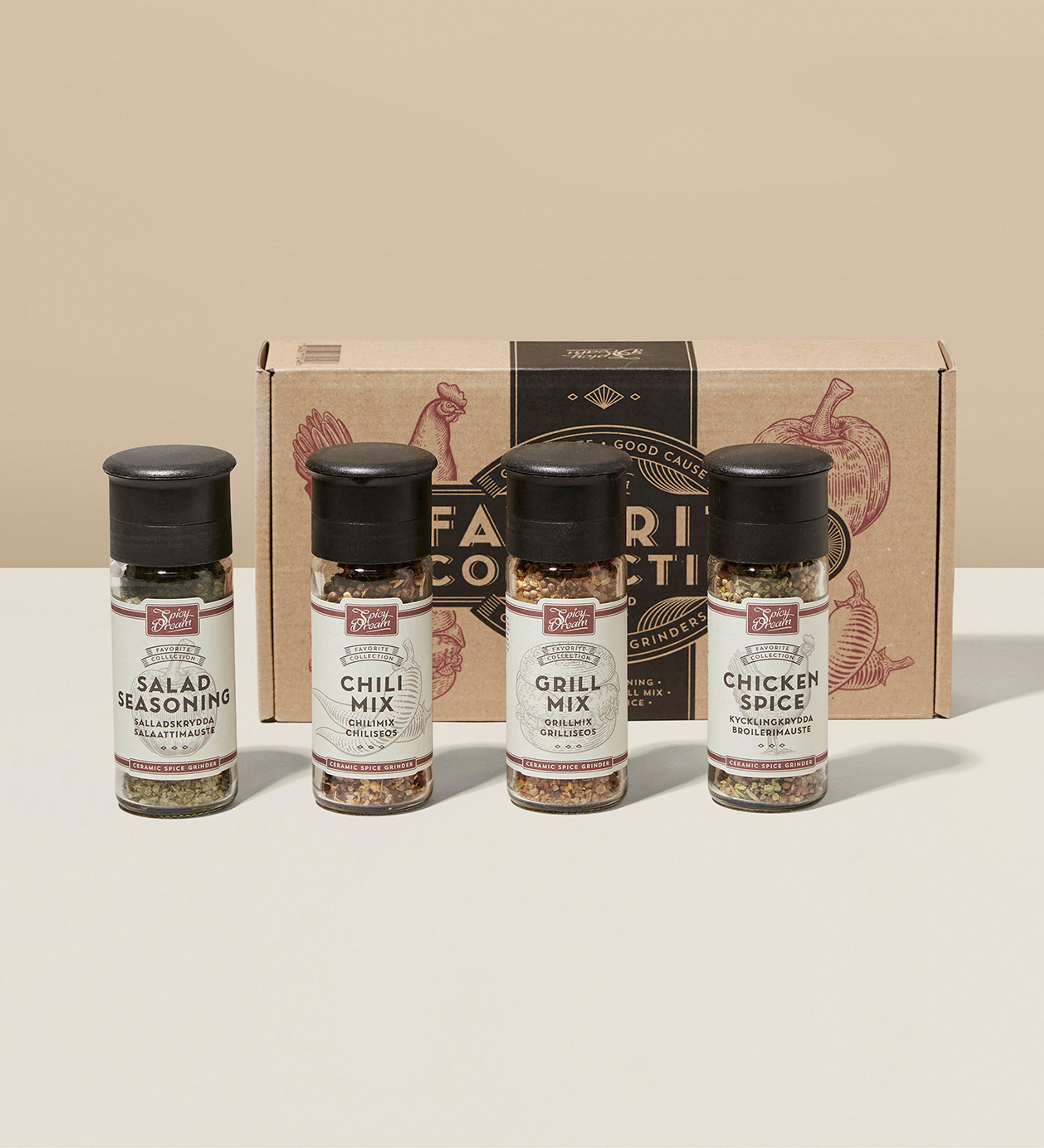 Fyra kryddkvarnar med smaker för sallad, chili, grill och kyckling framför en beige kartong med illustrationer av grönsaker och kyckling. Små, praktiska kryddburkar med svart lock och vit etikett.