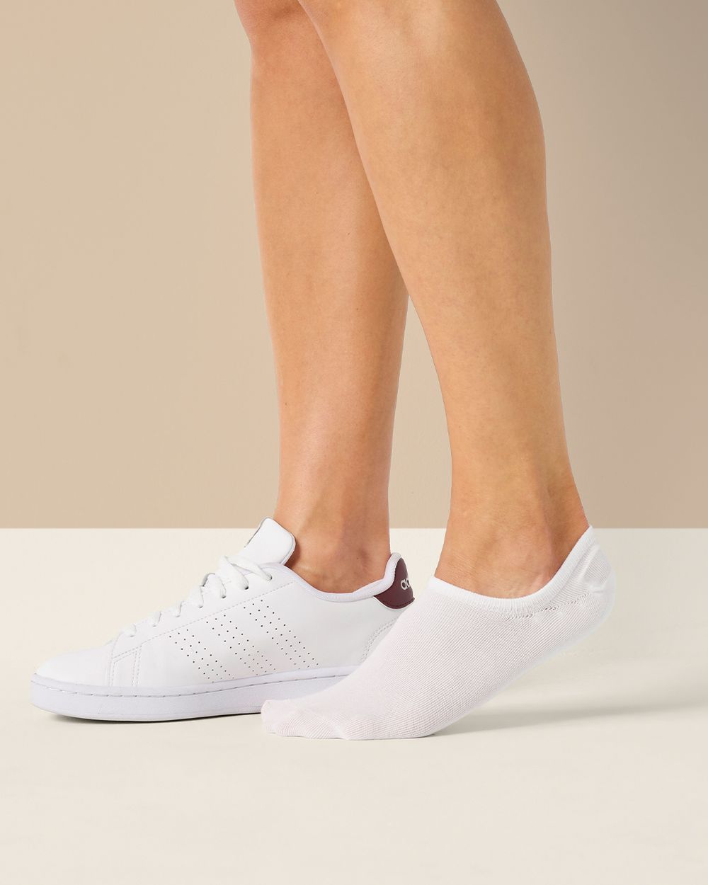 Vita tunna strumpor i en låg, osynlig modell, tillsammans med en vit sneaker med detaljer i mörkrött. Strumporna sitter bekvämt under foten och syns knappt när man har skor på.