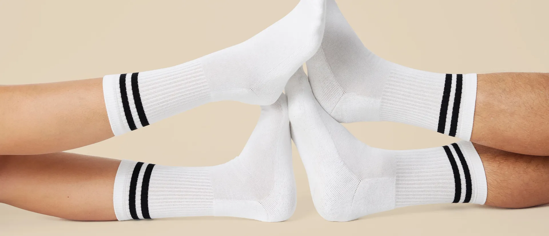 Fyra vita sportstrumpor med två svarta ränder runt vristen, visade på fötter som möts mot varandra. Strumporna är ribbstickade och når en bit upp på vaden.