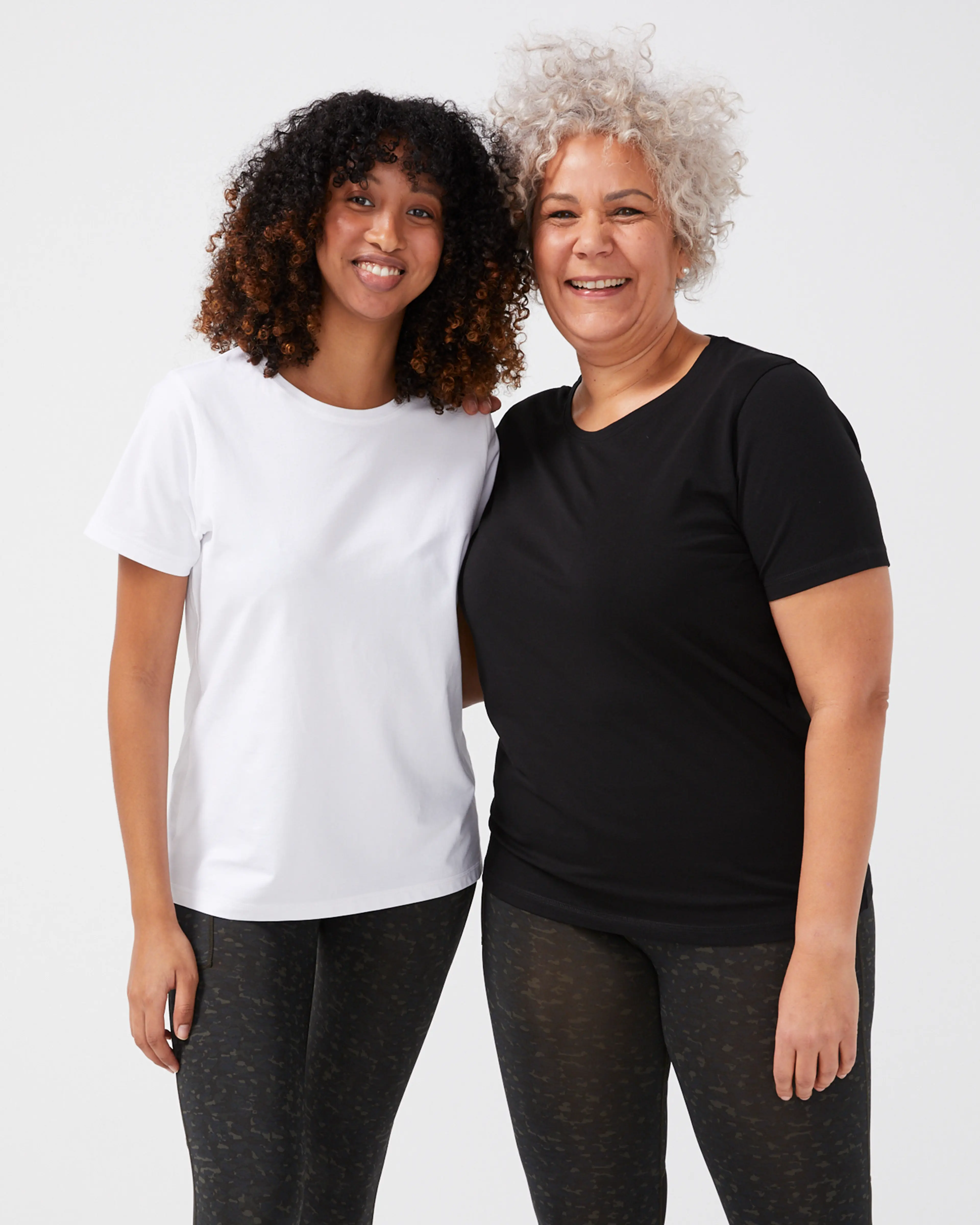 Två kvinnor i enkla t-shirts, en vit och en svart, båda med rund hals och kort ärm, i en vanlig passform.