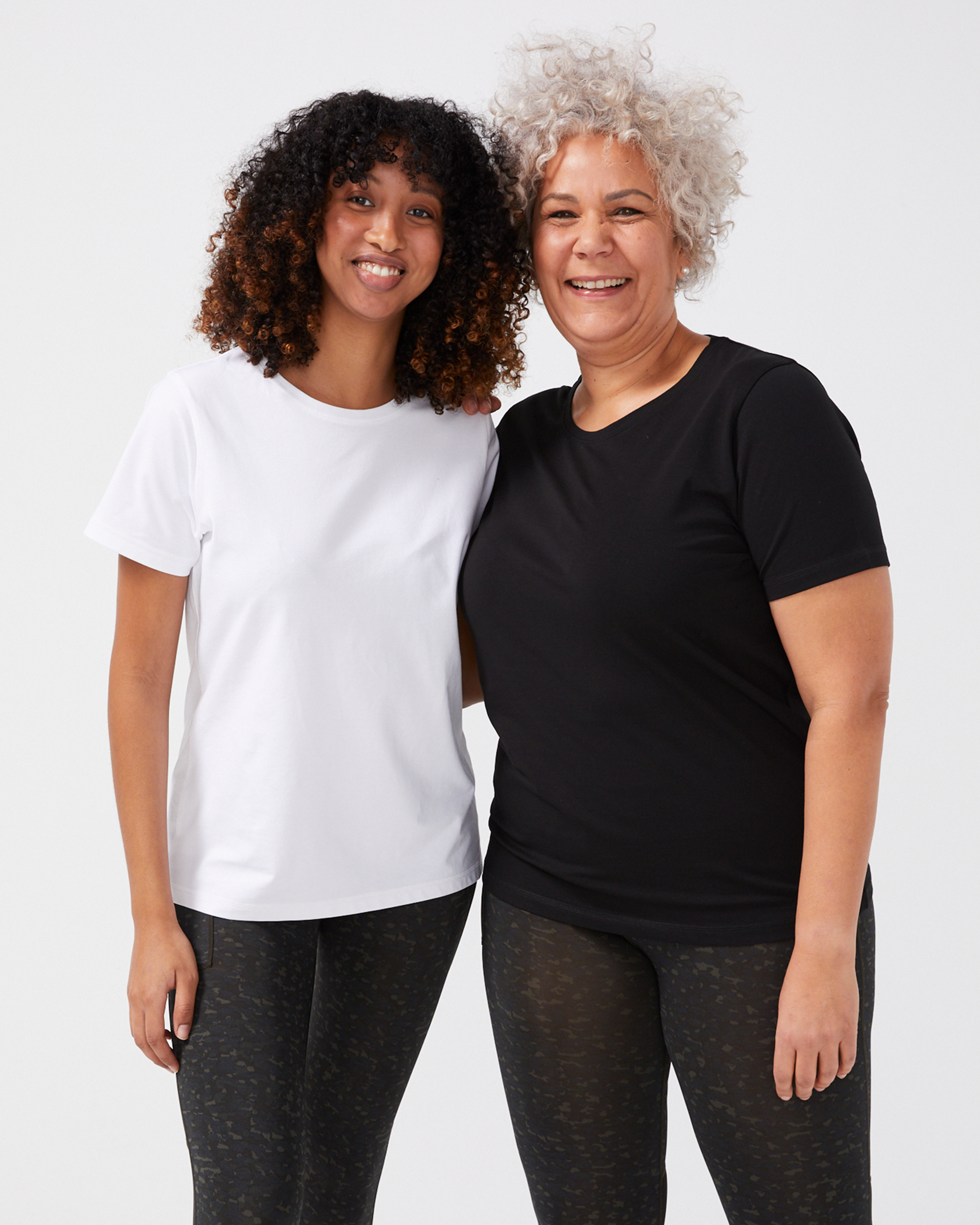 Två kvinnor i enkla t-shirts, en vit och en svart, båda med rund hals och kort ärm, i en vanlig passform.