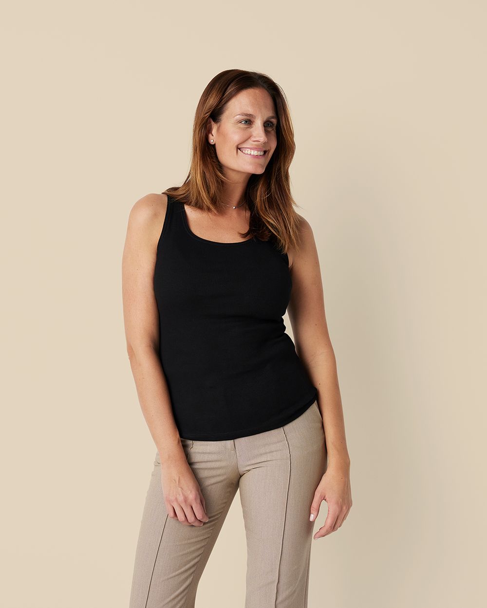 En svart ribbad linne-topp i smal passform, bärs av en leende kvinna med beige byxor. Toppen har en enkel och bekväm design perfekt för vardagsbruk.