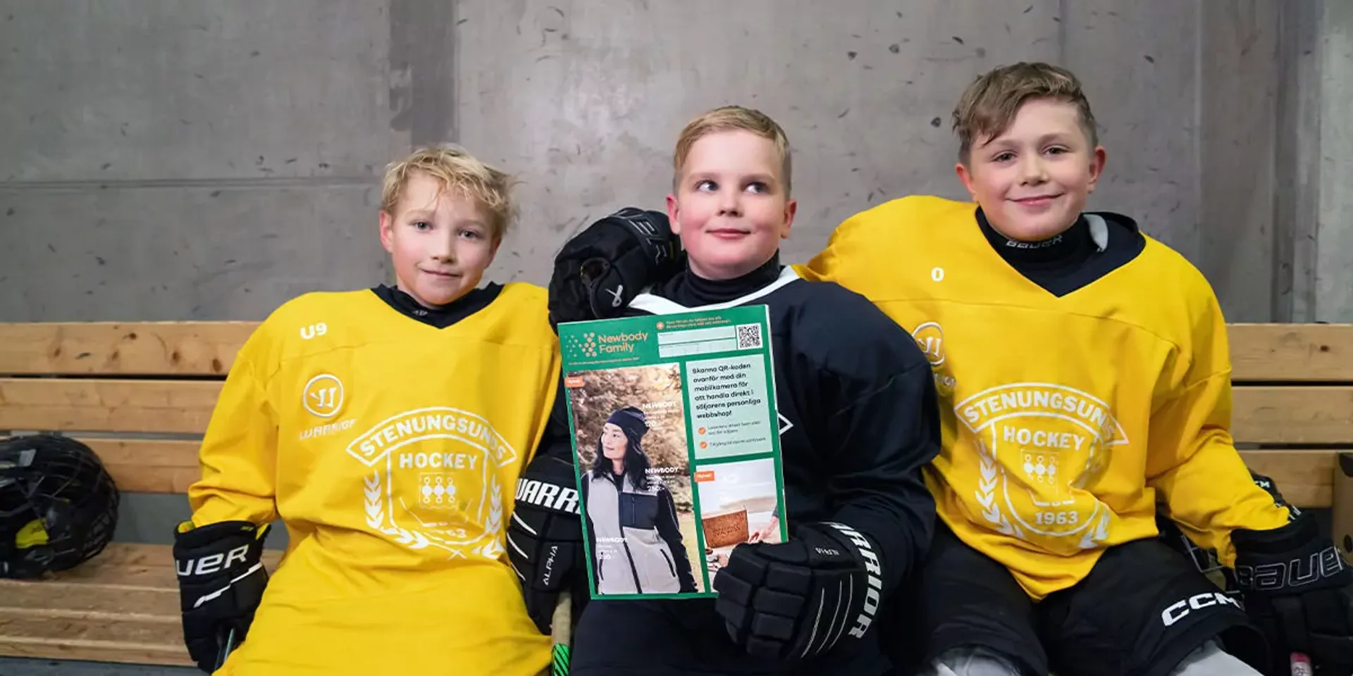 Tre glada hockeypojkar i gula och svarta tröjor sitter på en bänk i omklädningsrummet. Mitt i gruppen håller pojken i mitten upp en färgglad katalog.