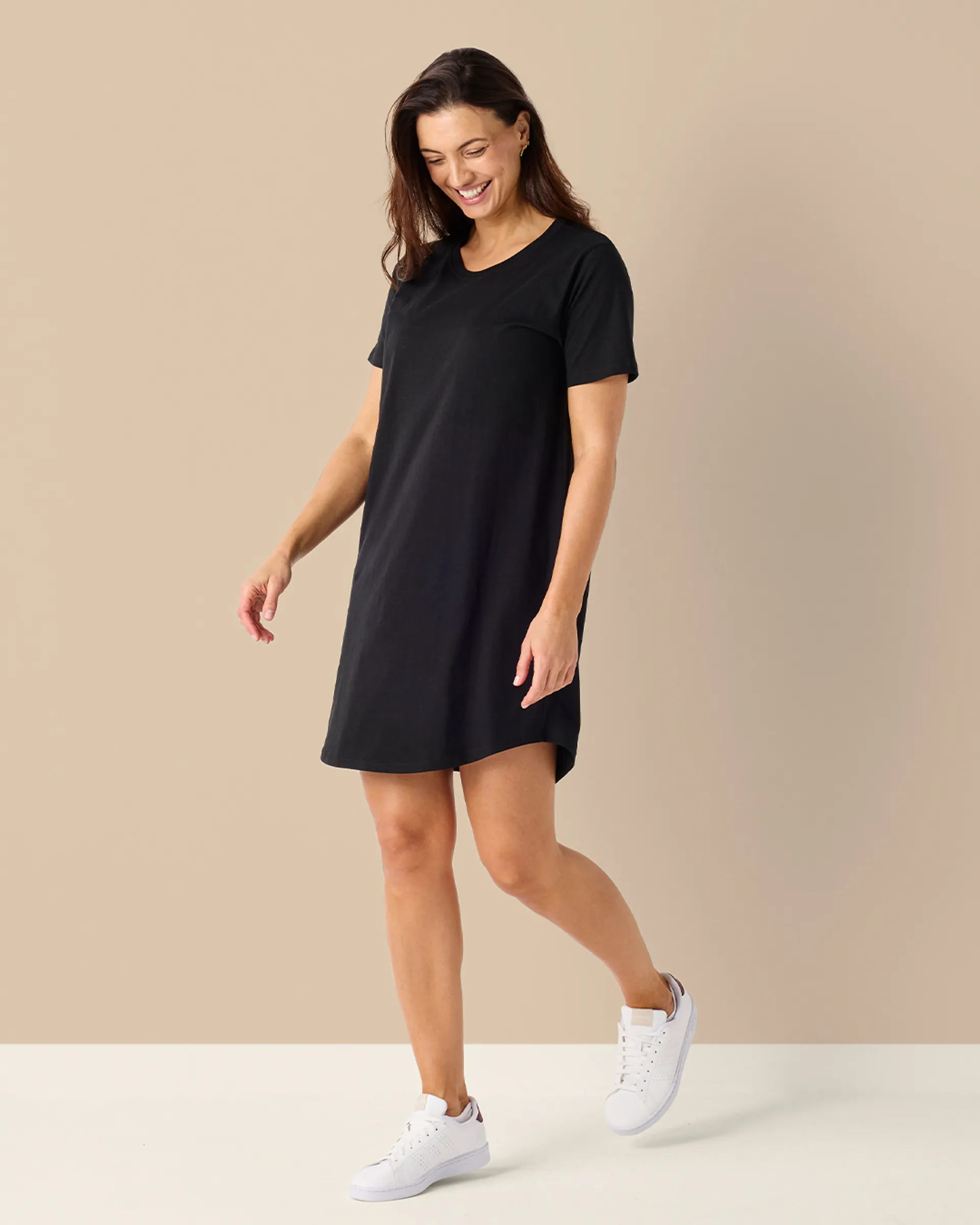 Svart, enkel t-shirtklänning med korta ärmar, bärs tillsammans med vita sneakers. Klänningen har en rak och bekväm passform som slutar ovanför knäna.