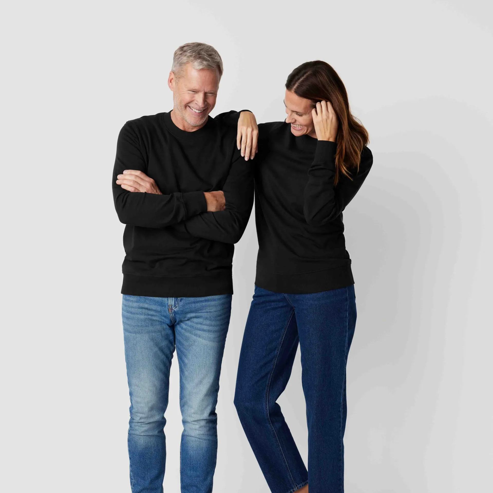 Svarta sweatshirts i enkel, klassisk design, bärs av en man och en kvinna med jeans. Sweatshirtsen har ribbstickade ärmslut och fåll.