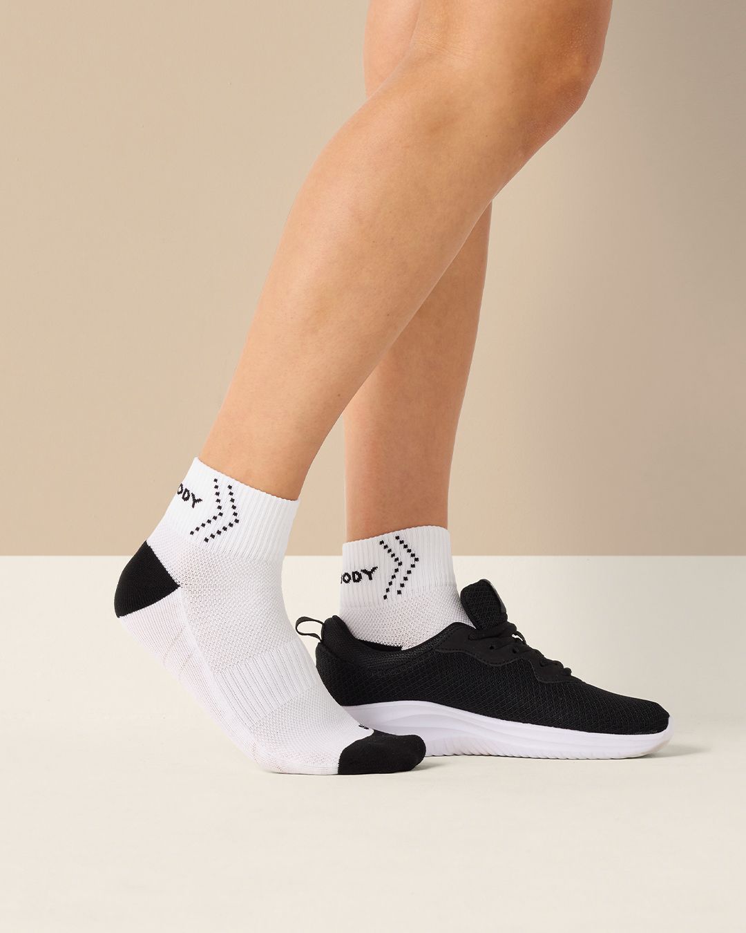 Vita sportstrumpor med svart häl och tå, med ett lätt vadderat och ventilerande material. En fot bär strumpan och den andra har en svart löparsko med vit sula.