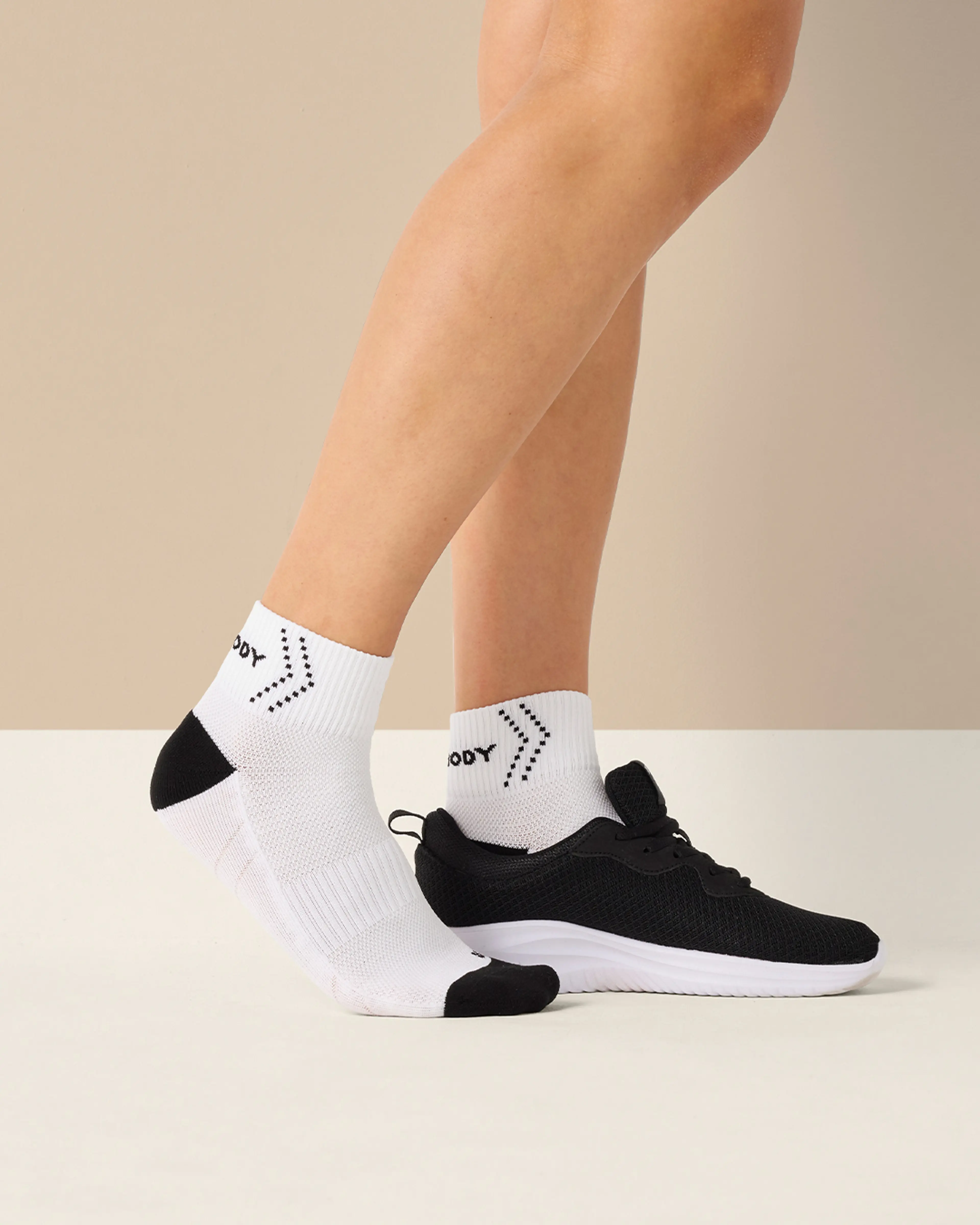 Vita sportstrumpor med svart häl och tå, med ett lätt vadderat och ventilerande material. En fot bär strumpan och den andra har en svart löparsko med vit sula.