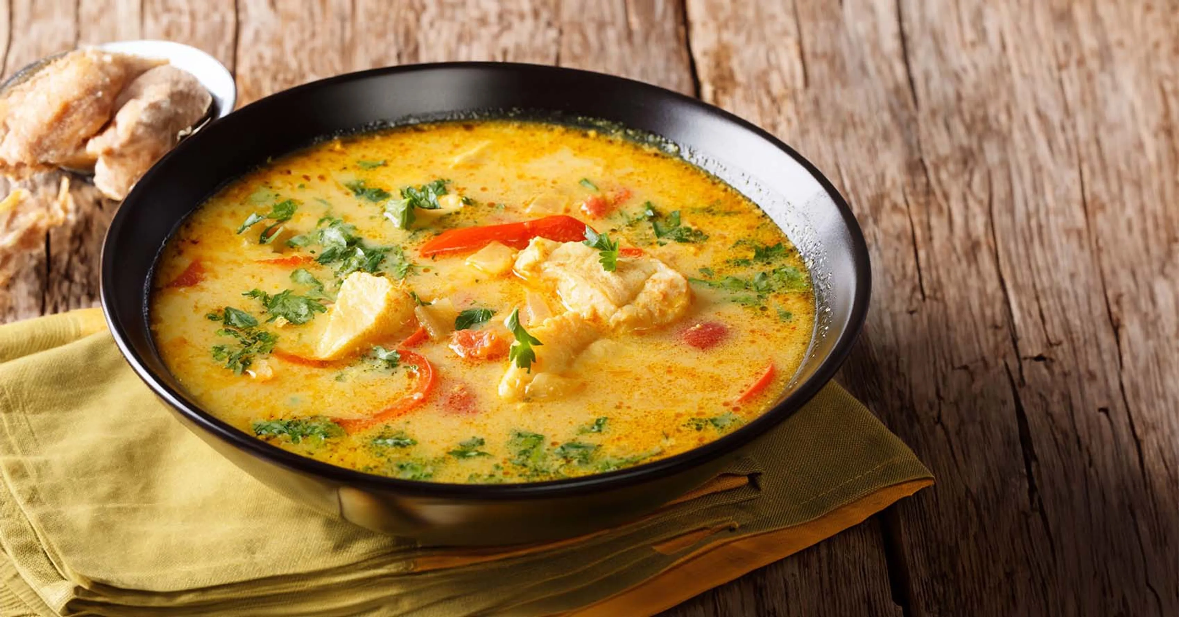 Krämig fisksoppa med saffran, röda paprikabitar och färsk persilja i en svart skål. Sopppan har en varm, gyllene färg med bitar av vit fisk.