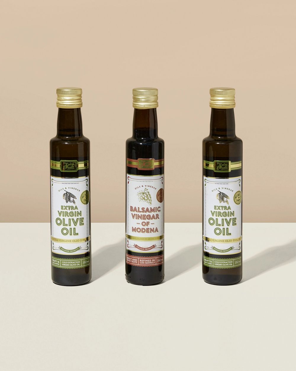 Tre flaskor med olja och vinäger; två med extra jungfruolivolja och en med balsamvinäger av Modena, alla i mörka glasflaskor med guldlock.