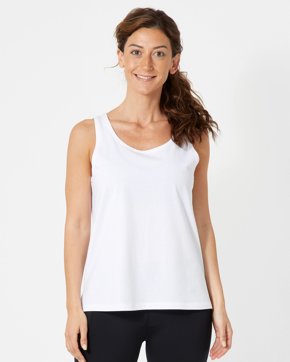 En enkel vit tanktop med normal passform, utan mönster eller detaljer. Modellen bär den tillsammans med svarta byxor för en avskalad och bekväm stil.