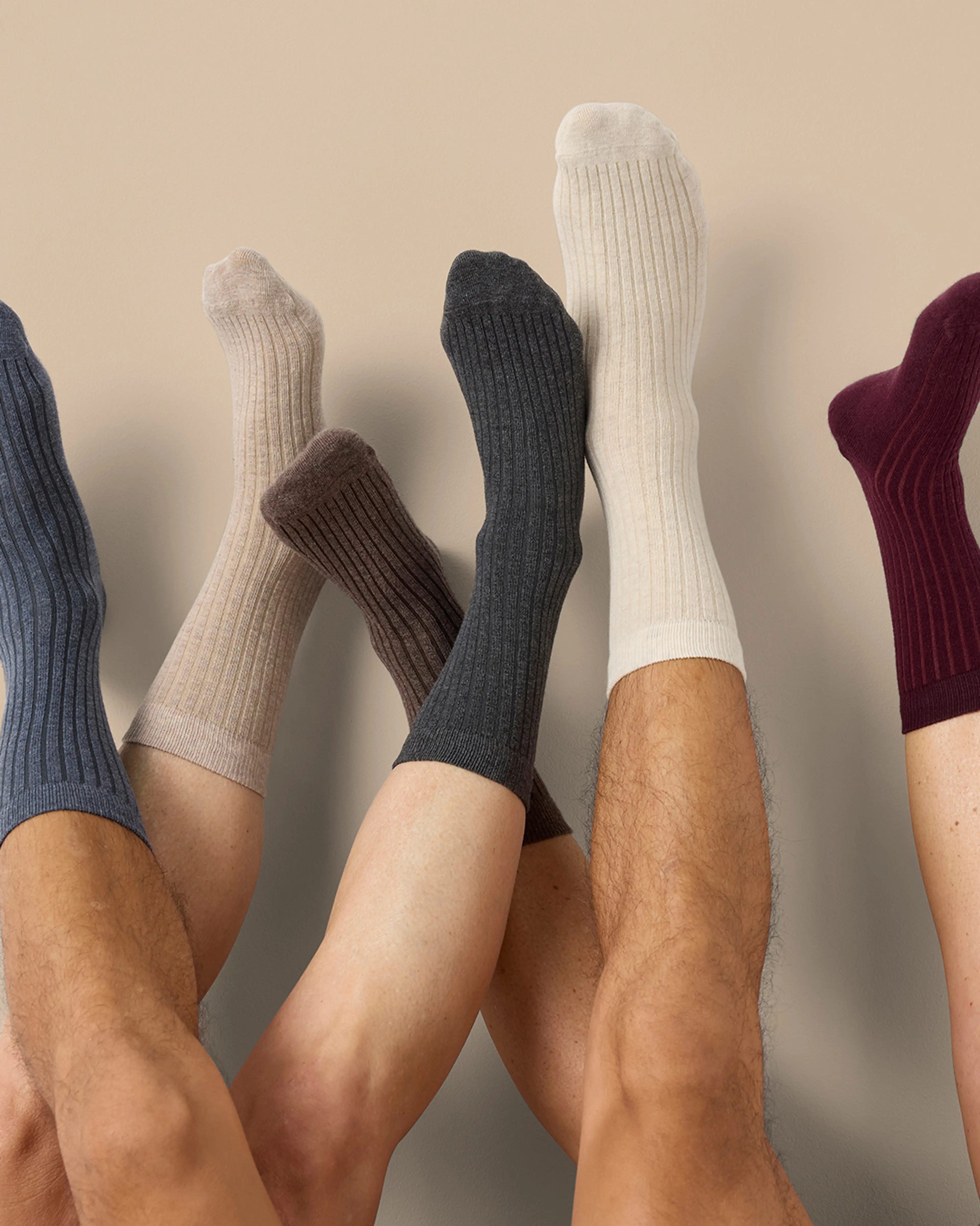 Fem par ribbade strumpor i olika jordnära färger som mörkblått, beige, brunt, mörkgrått, vitt och vinrött. Strumporna sitter på upplyfta ben mot en ljus bakgrund.