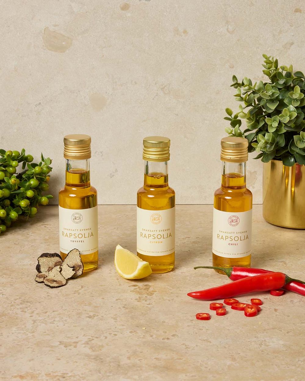 Tre flaskor smaksatt rapsolja med tryffel, citron och chili i en inspirerande köksmiljö.