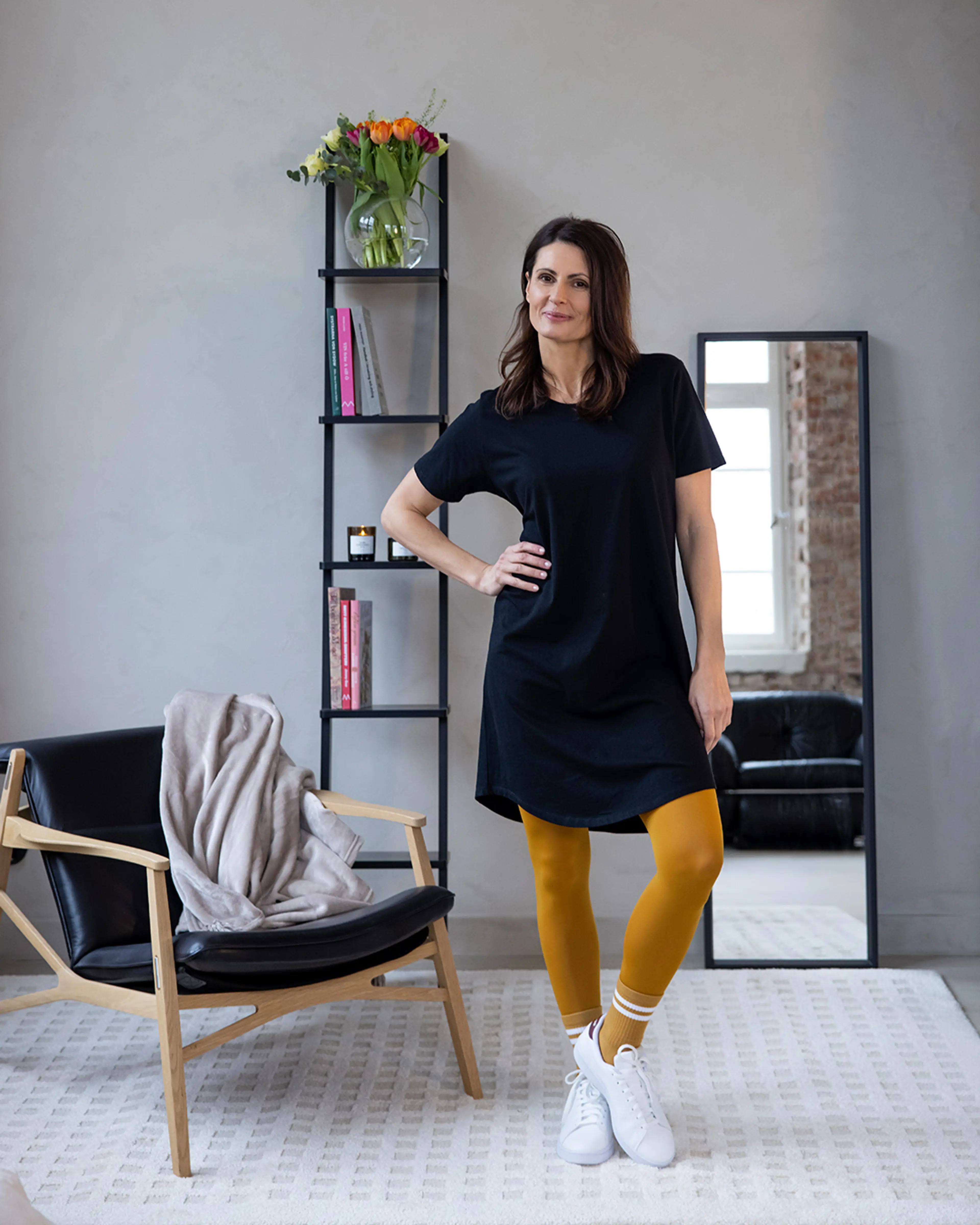 En enkel, svart t-shirtklänning i avslappnad modell, kombinerad med senapsgula leggings och vita sneakers. En modern och bekväm vardagslook.