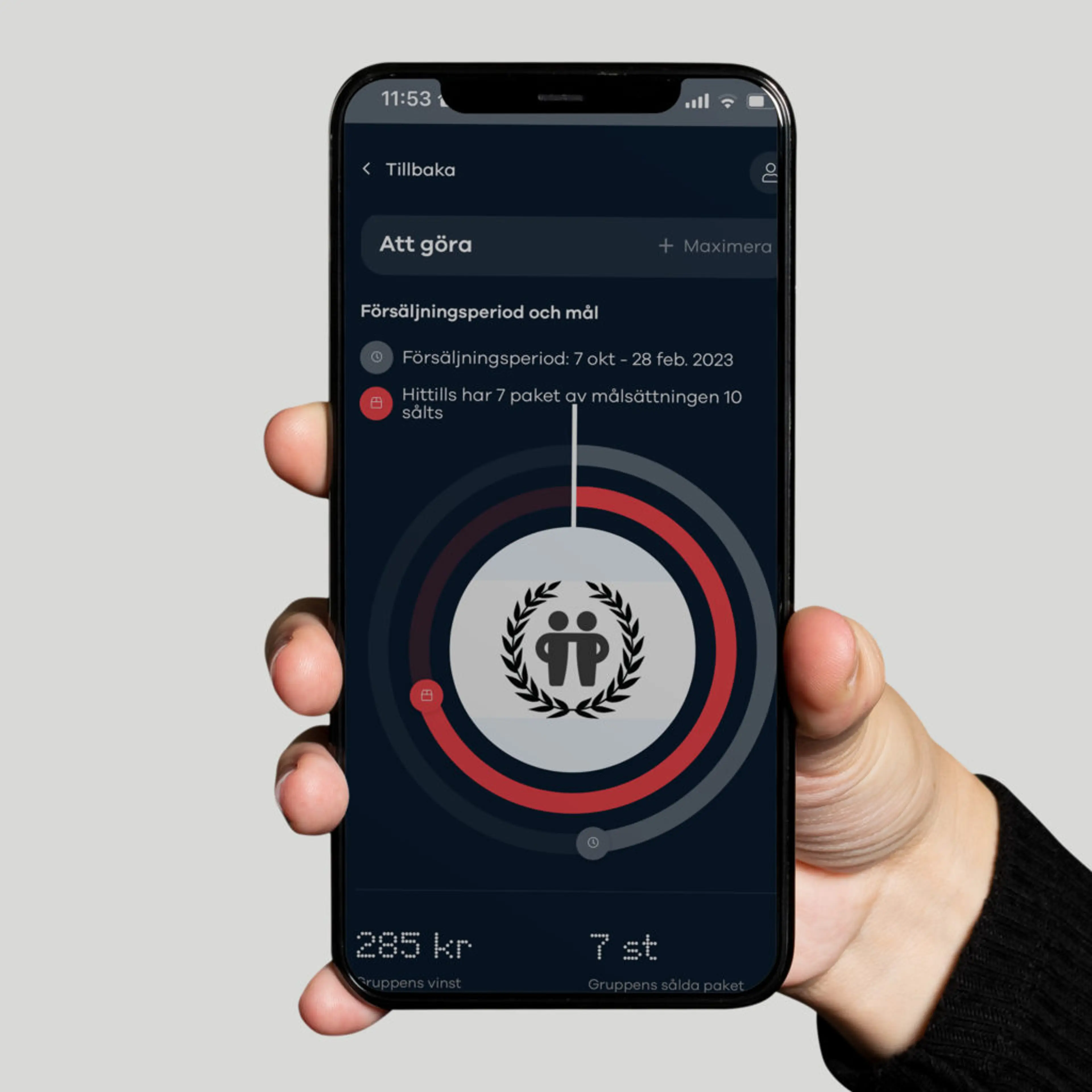En hand håller en mobiltelefon som visar en försäljningsapp med en cirkeldiagram över målsättning och sålda paket. Skärmen visar att 7 av 10 paket har sålts under försäljningsperioden 7 okt – 28 feb 2023.