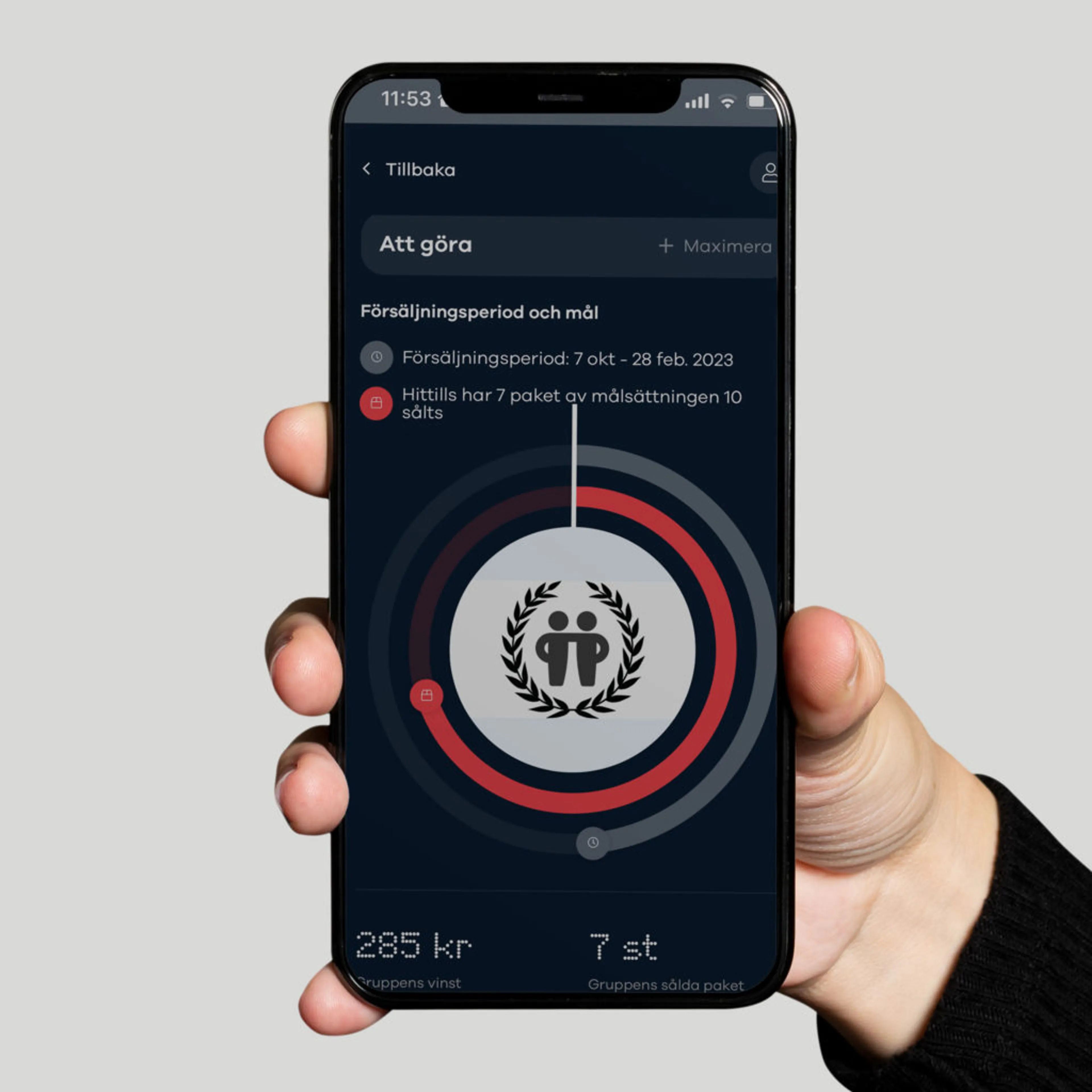 En hand håller en mobiltelefon som visar en försäljningsapp med en cirkeldiagram över målsättning och sålda paket. Skärmen visar att 7 av 10 paket har sålts under försäljningsperioden 7 okt – 28 feb 2023.