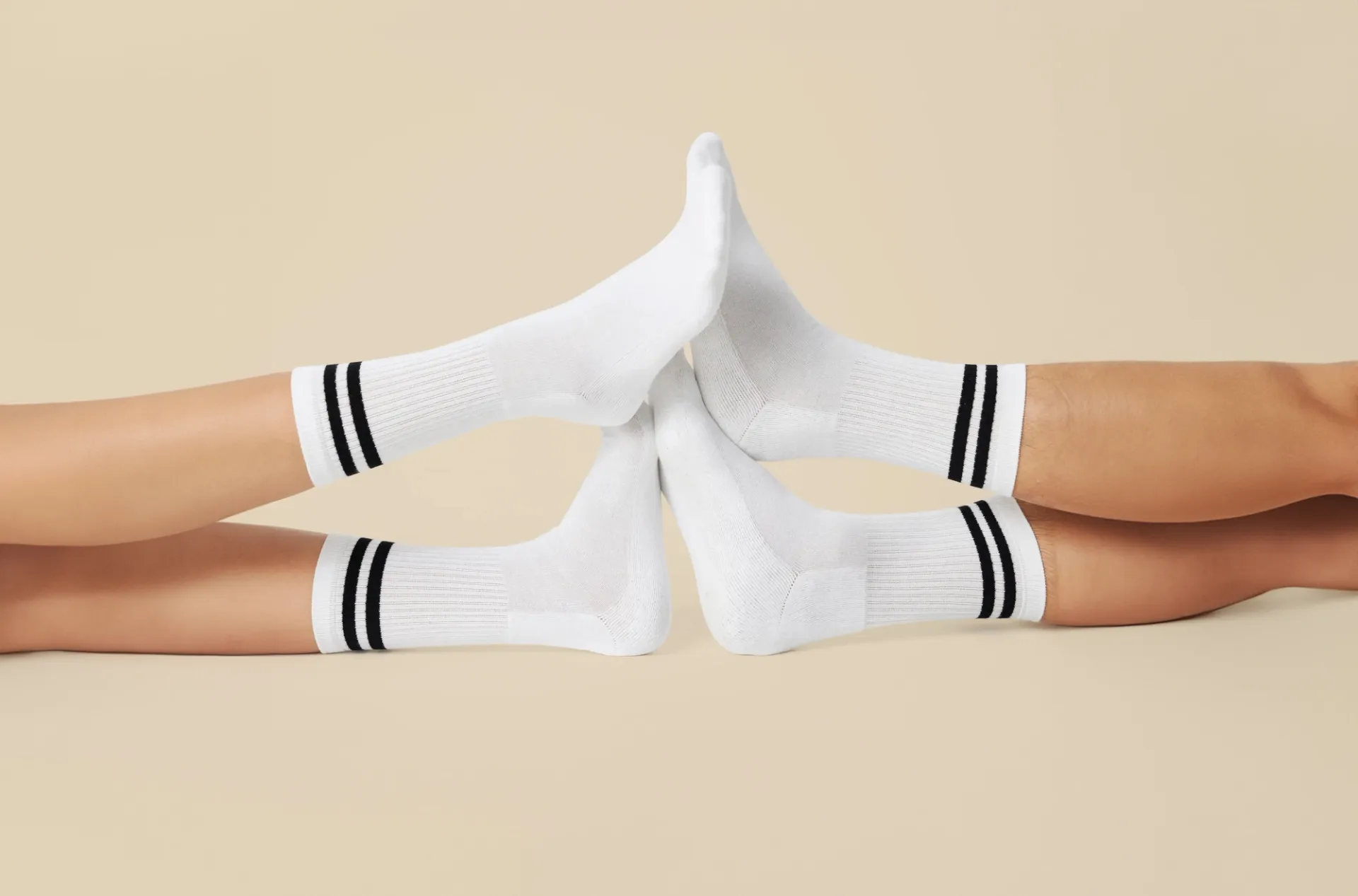 Fyra vita sportstrumpor med två svarta ränder runt vristen, visade på fötter som möts mot varandra. Strumporna är ribbstickade och når en bit upp på vaden.