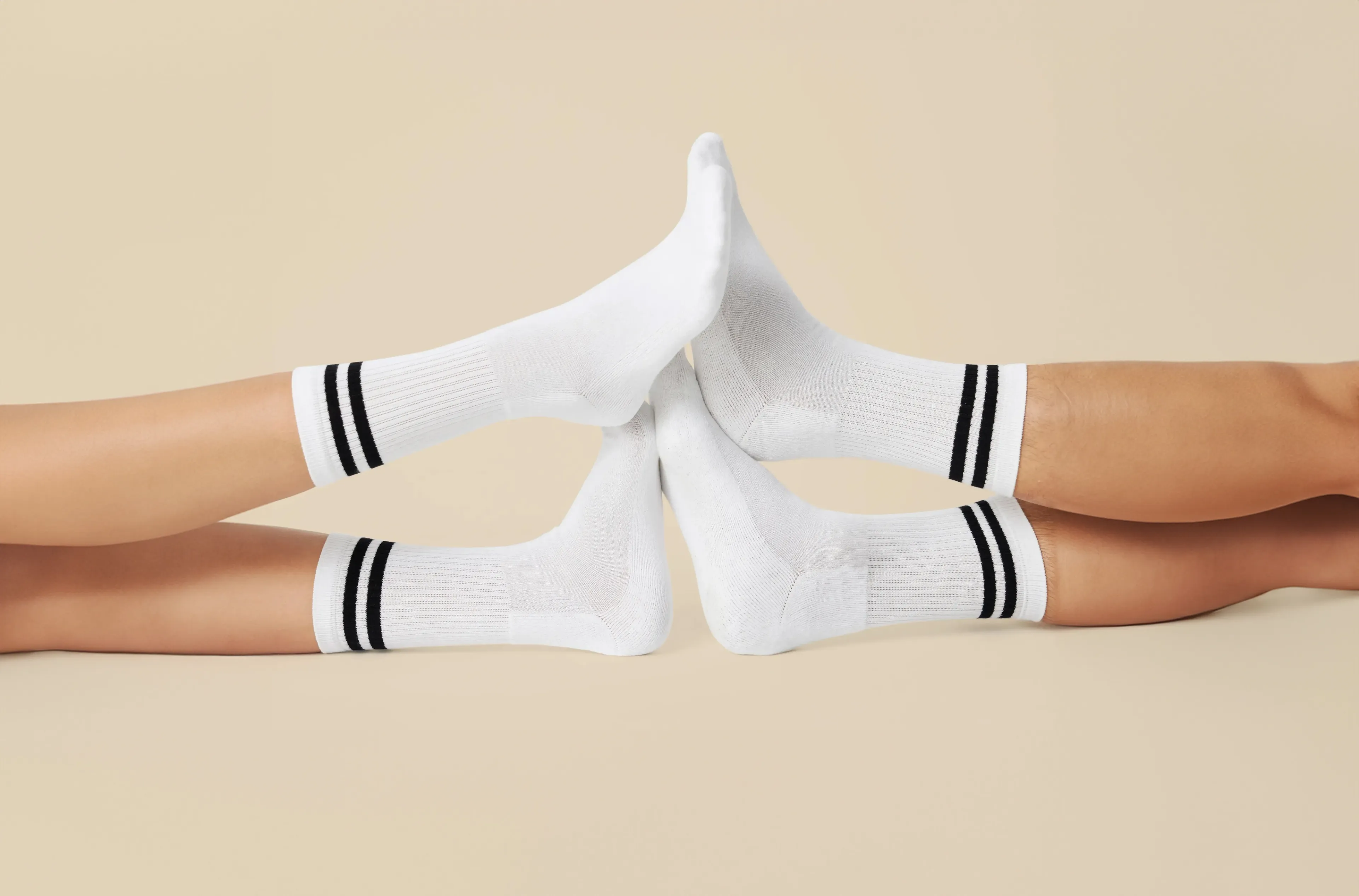 Fyra vita sportstrumpor med två svarta ränder runt vristen, visade på fötter som möts mot varandra. Strumporna är ribbstickade och når en bit upp på vaden.