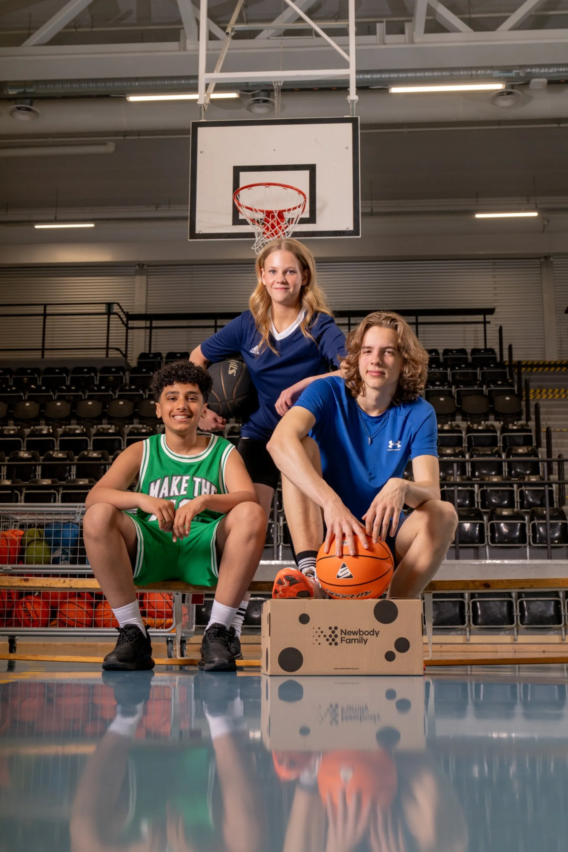 Tre basketspelare med en basketboll och en Newbody kartong