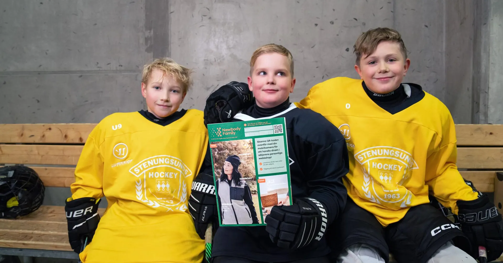 Tre ishockeykillar sitter i avbytarbåset med en Newbody katalog i handen.