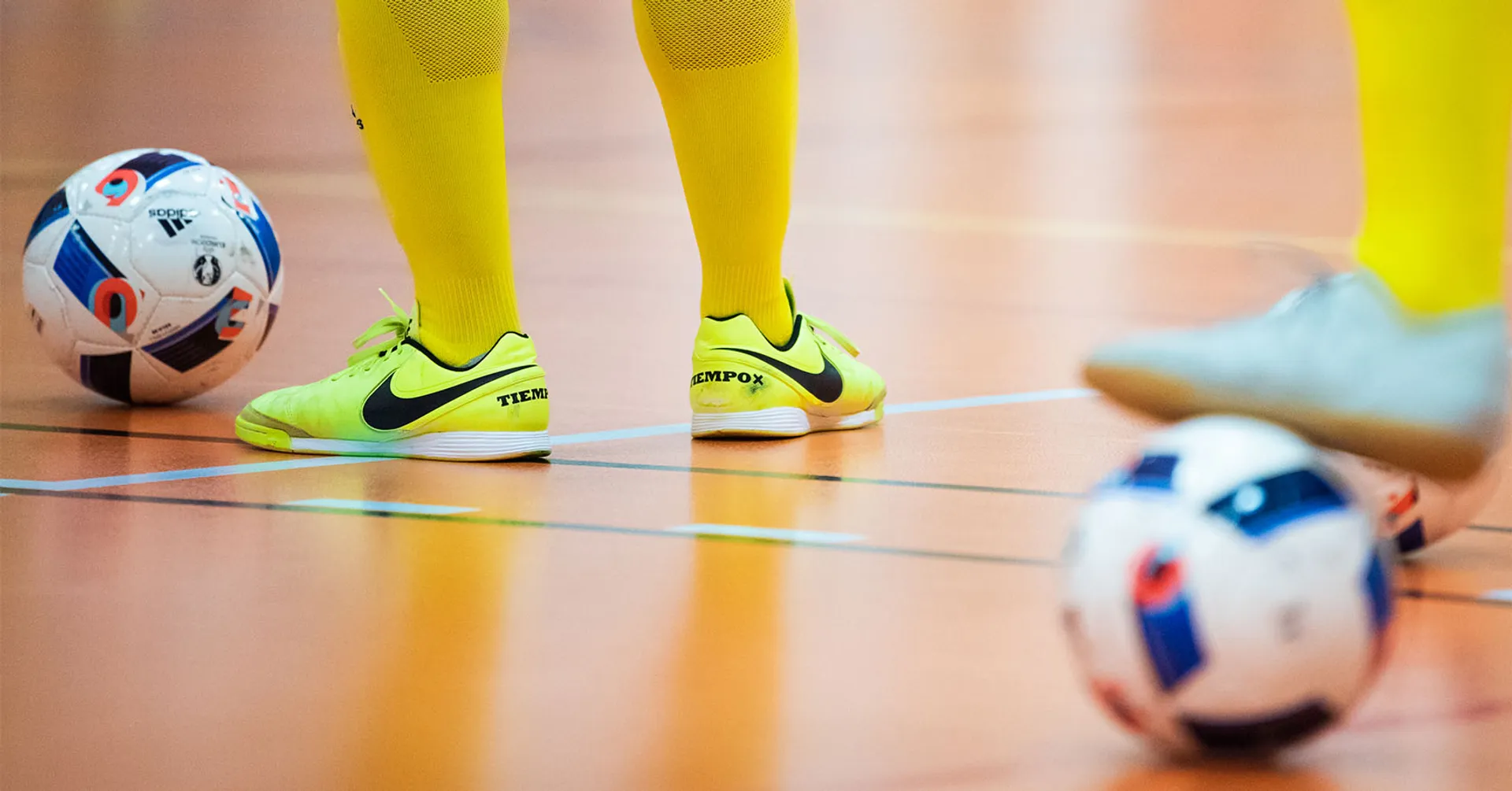 benen på två futsal spelare med gula höga strumpor, fotbollsskor och varsin fotboll