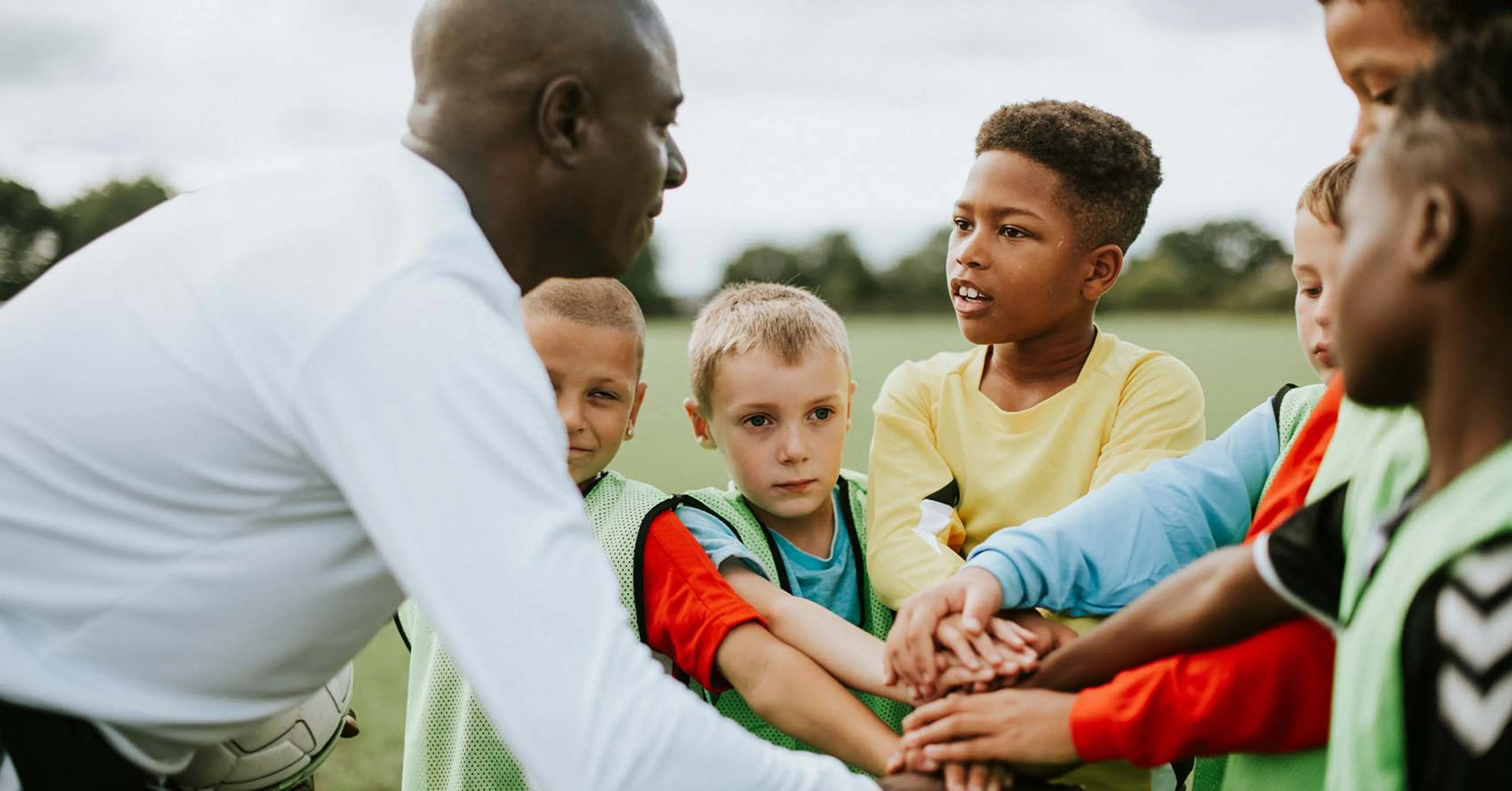 Fotbollsspelare som står i en ring tillsammans med sin tränare, de har händerna in i ringen