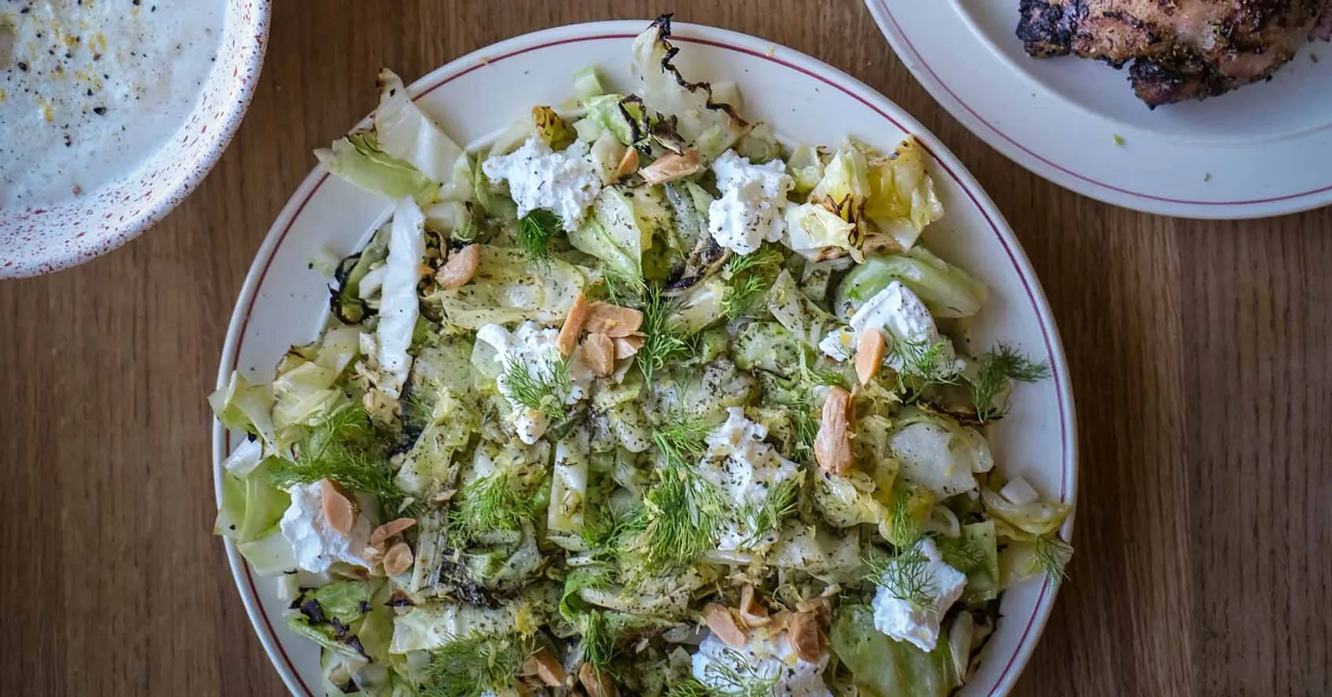 Grillad vitkål toppad med smulig ost, dill och rostad mandel på ett vitt fat. Färska örter och kryddor ger en fräsch och kryddig touch.