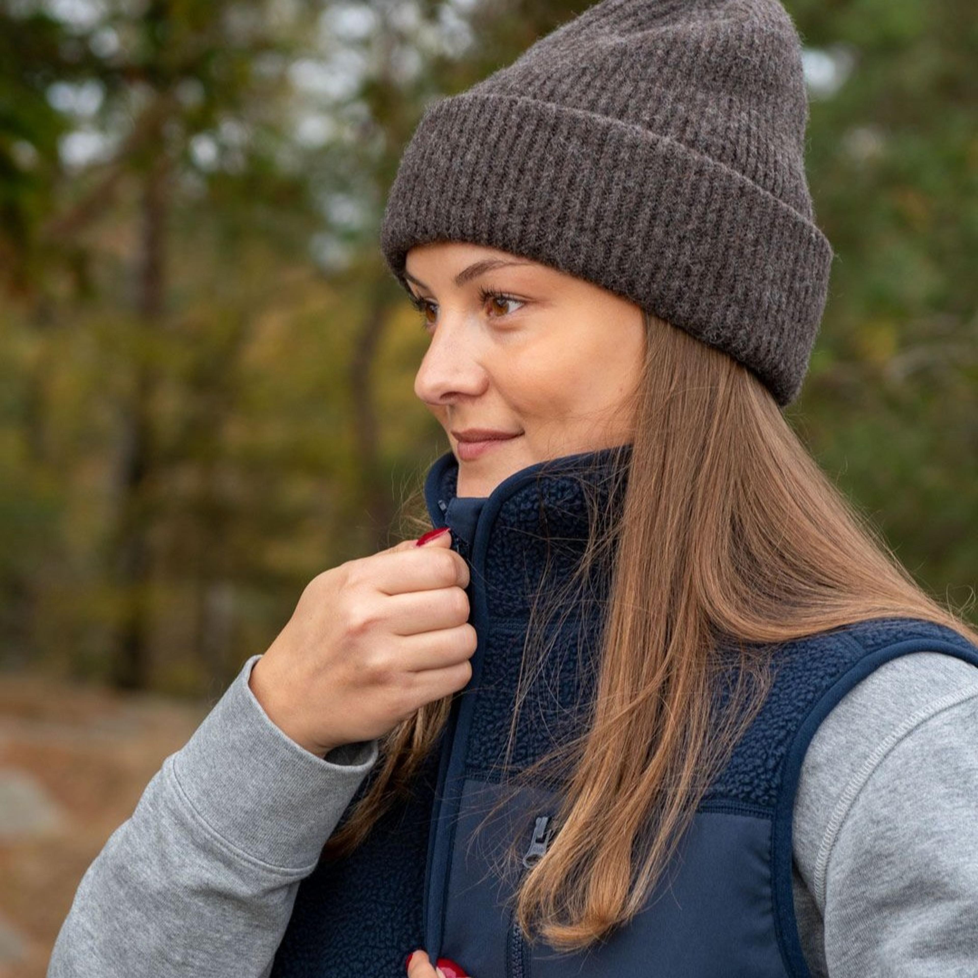 Tjej med brunt hår, brun mössa och en mörkblå flis väst
