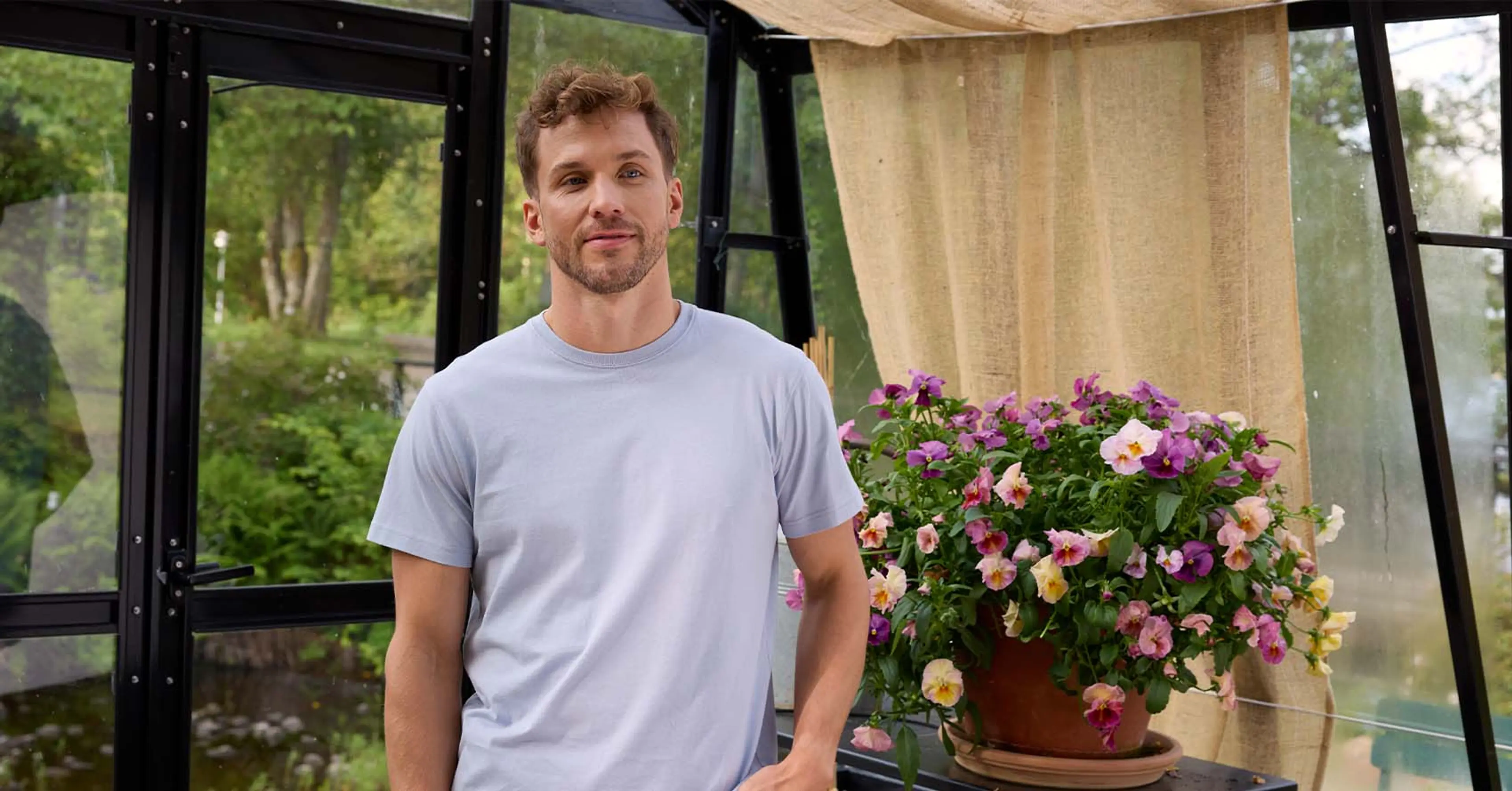 Man i ljusblå men's tshirt, ståendes i ett växthus