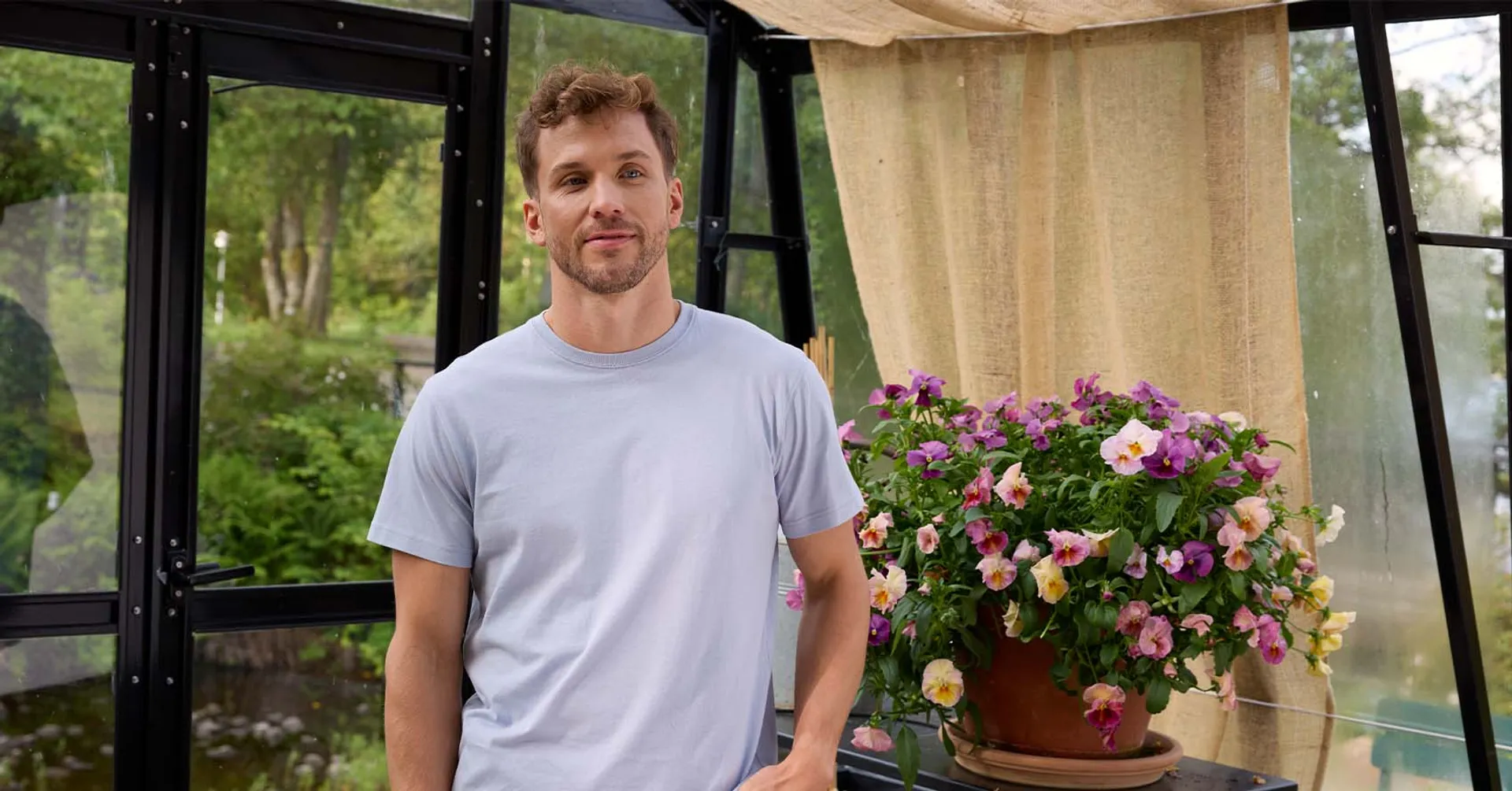 Man i ljusblå men's tshirt, ståendes i ett växthus