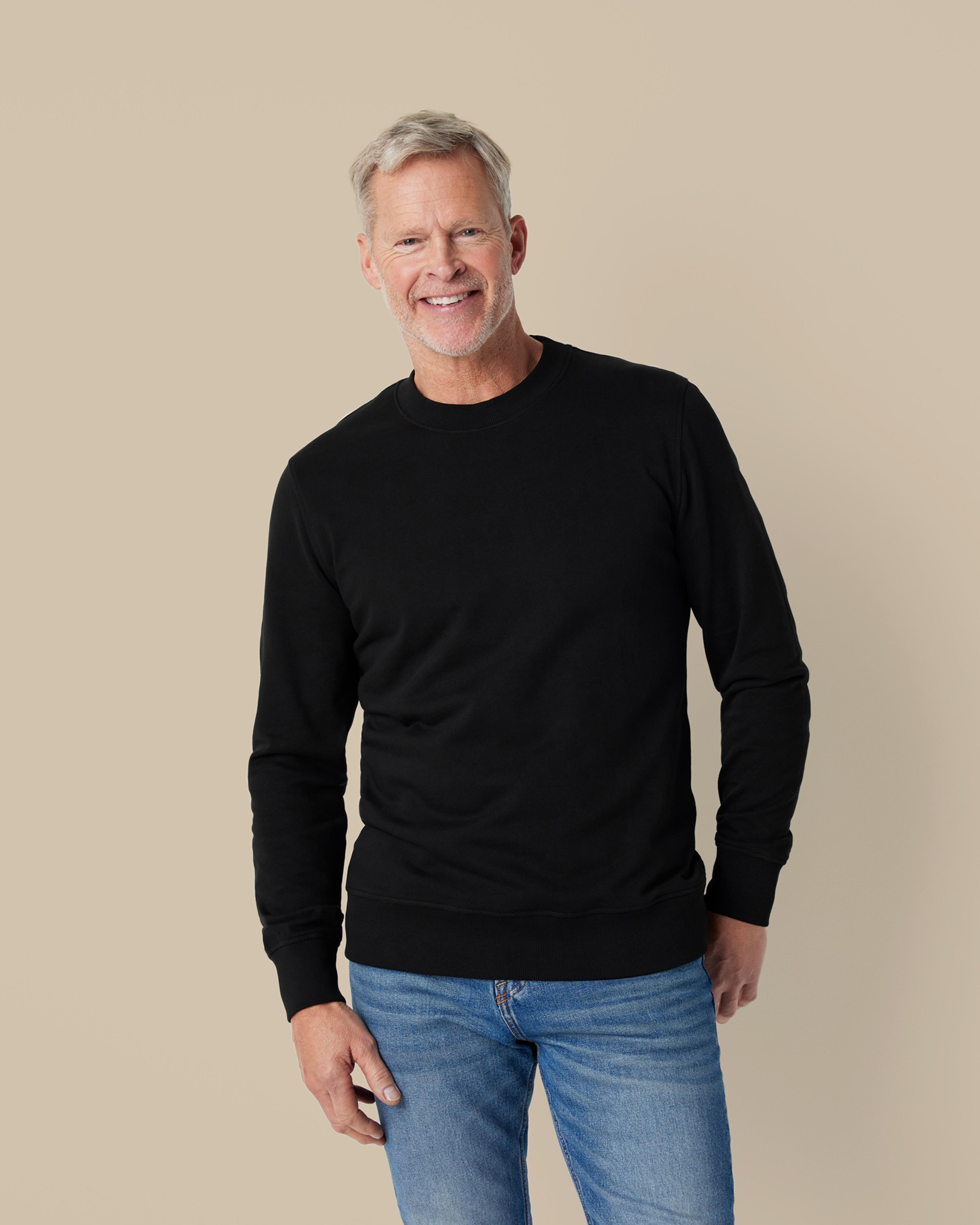 En svart sweatshirt med rund halsringning i en mjuk och enkel design, kombinerad med ett par ljusblå jeans. Tröjan har ribbstickade muddar vid ärmslut och nederkant.