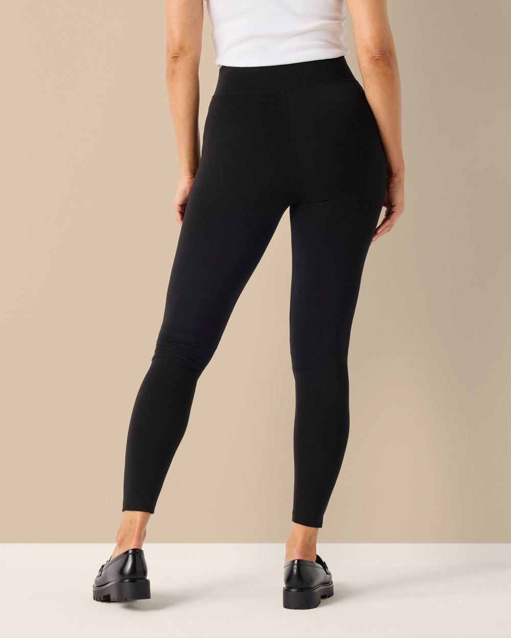 Svarta leggings i mjuk bomull med hög midja och smal passform. Modellen bär dem tillsammans med svarta loafers och en vit topp.