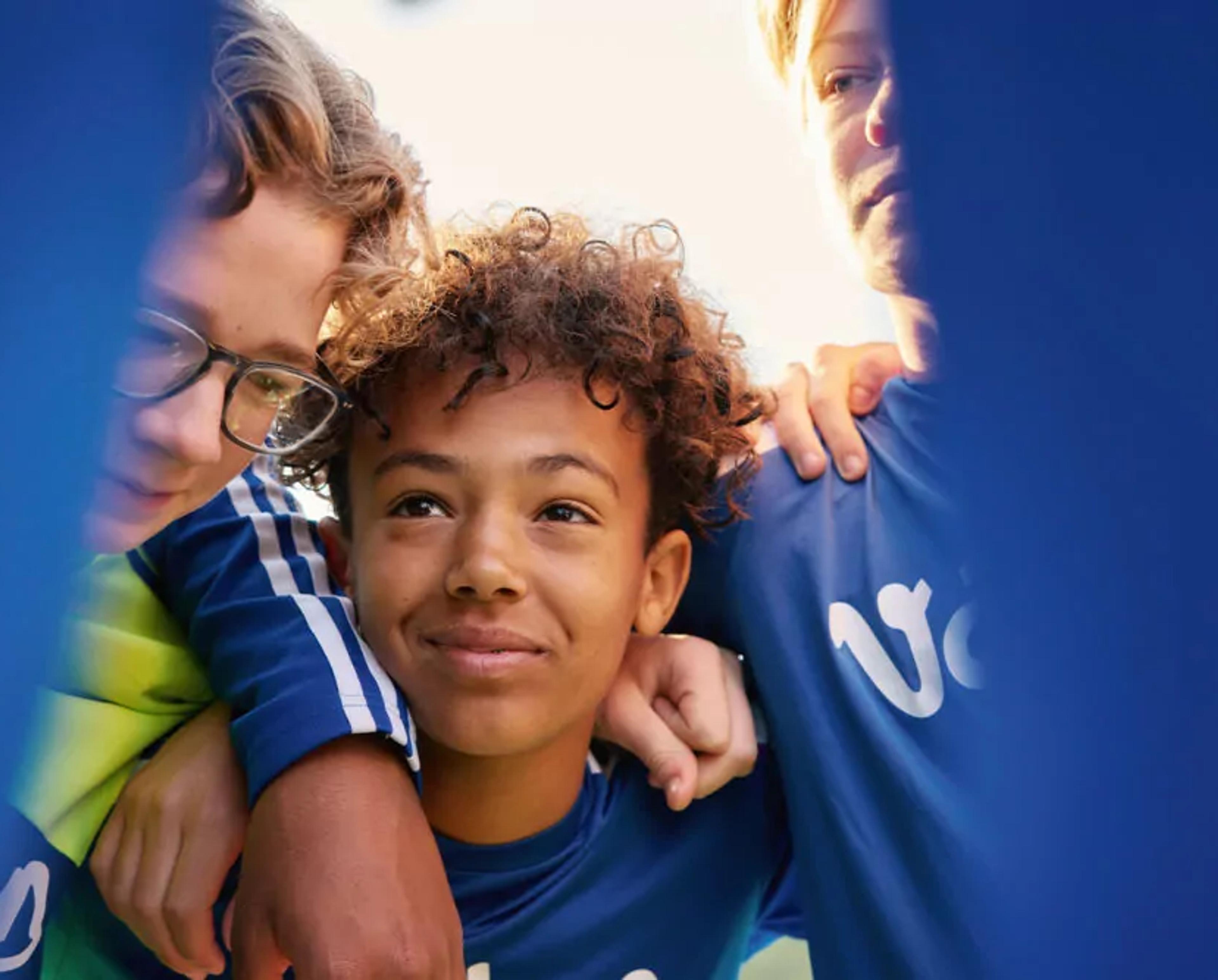 Tre ungdomar i blåa tröjor som står tätt tillsammans, ena personen har armen om en annan. De ser ut att dela en stund av samhörighet och stöd.