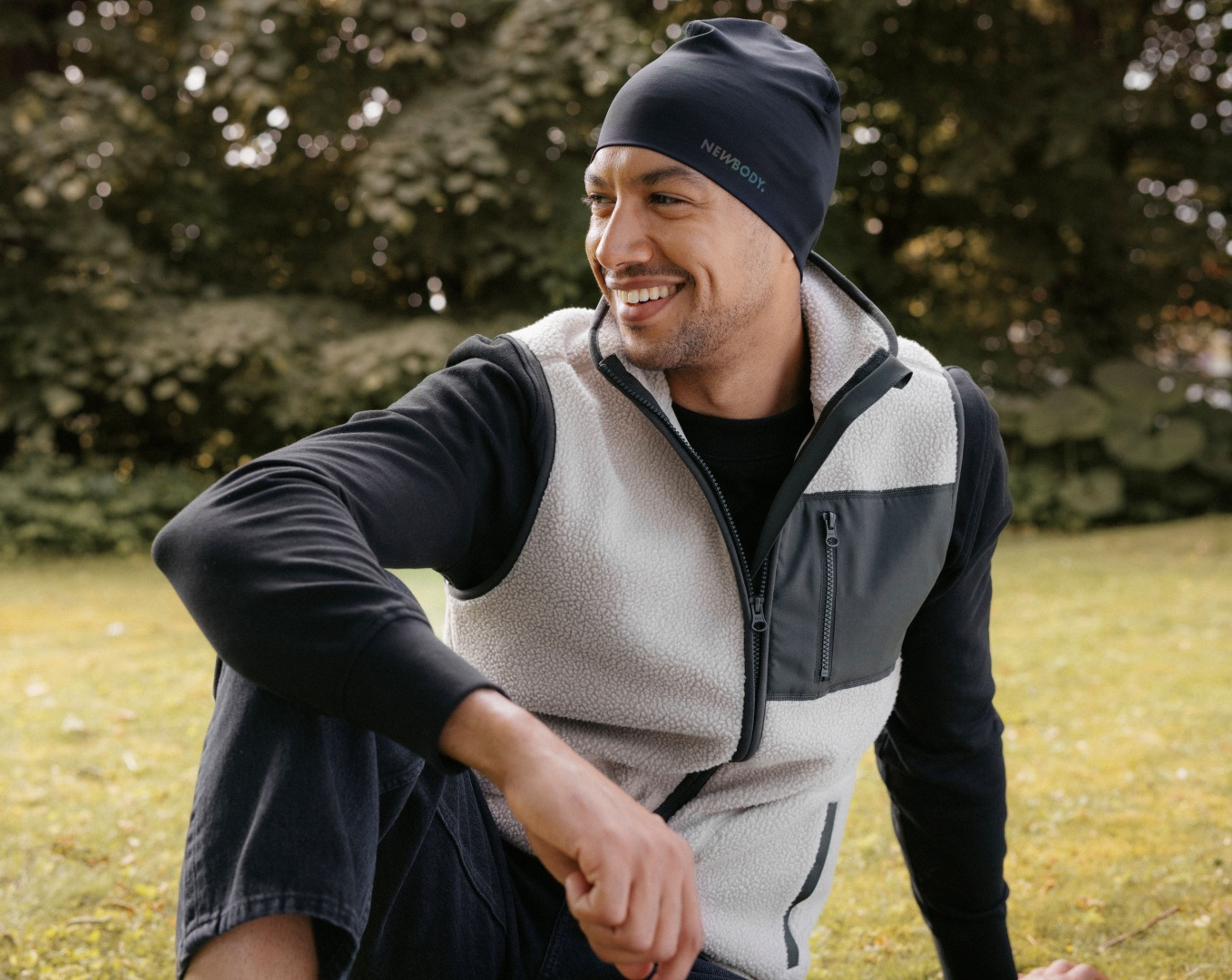 Man i mjuk beige pile vest med gröna detaljer, han sitter på en gräsmatta