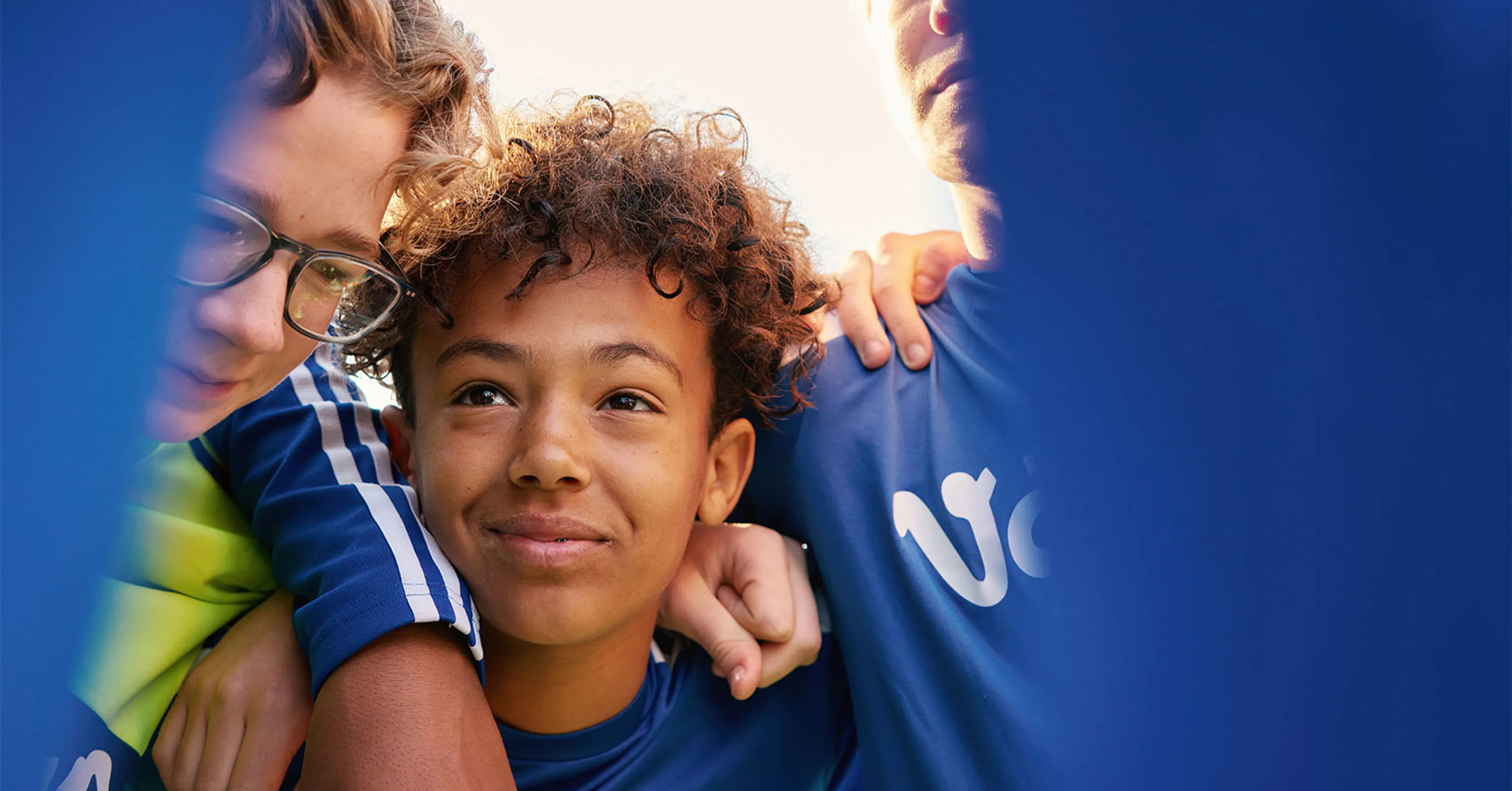 Tre fotbolls spelare med blå kläder som står och håller om varandra som ett lag