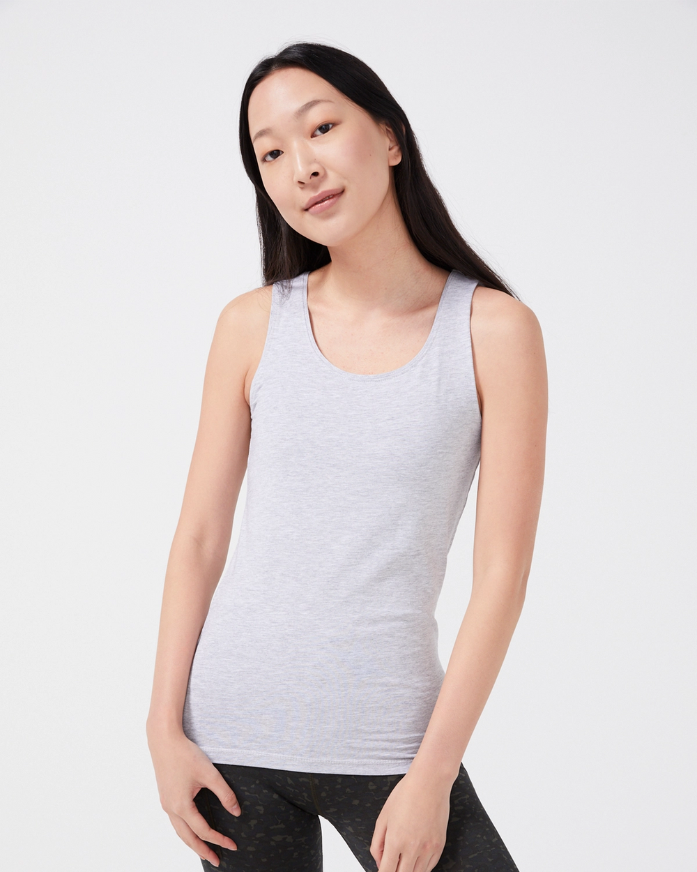 En ljusgrå melerad tanktop med breda axelband i en mjuk och enkel design. Modellen bär toppen tillsammans med mörka träningsleggings.