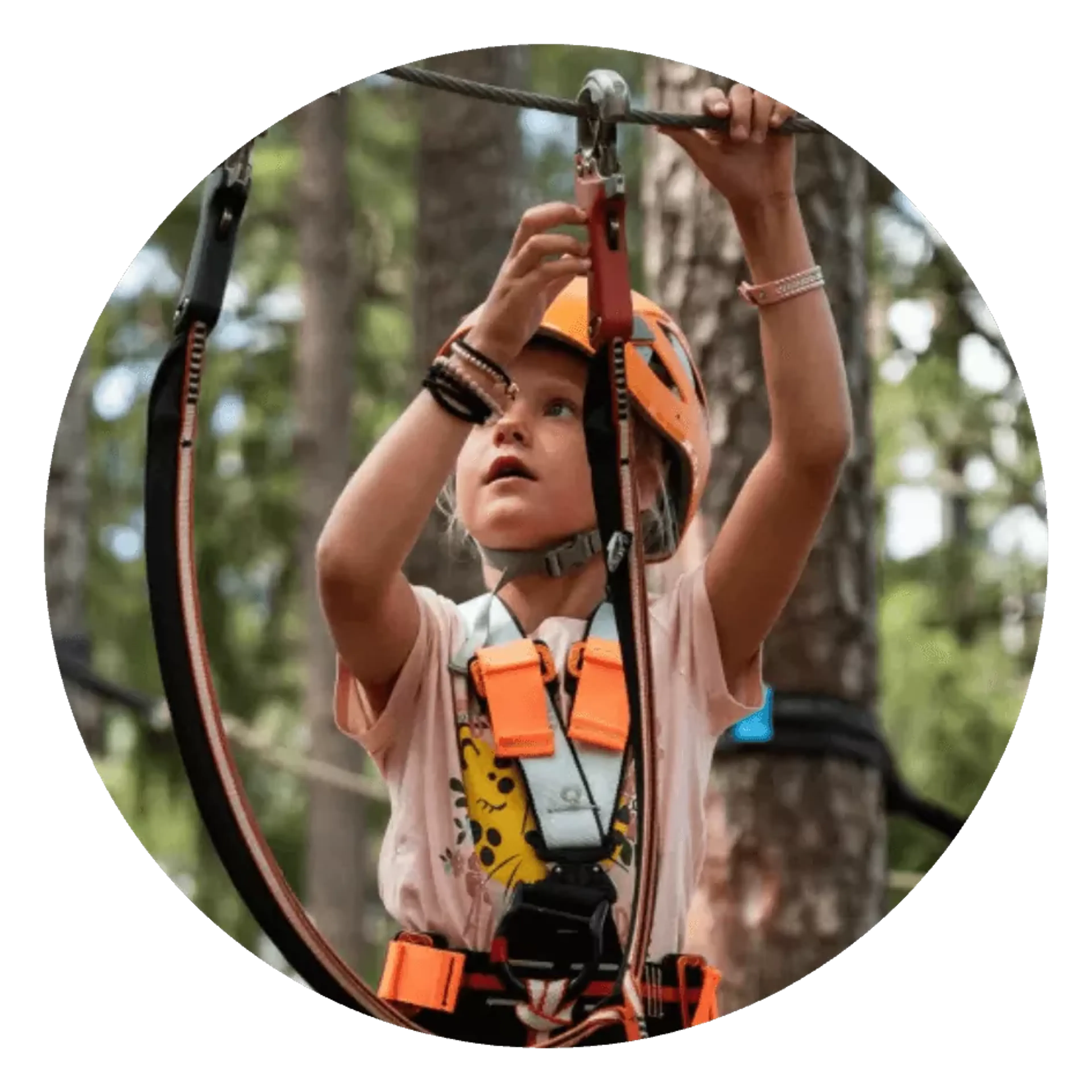Ett barn i orange klätterhjälm och sele fäster säkerhetsutrustning i en linbana i skogen. Bakgrunden visar träd och grönska.