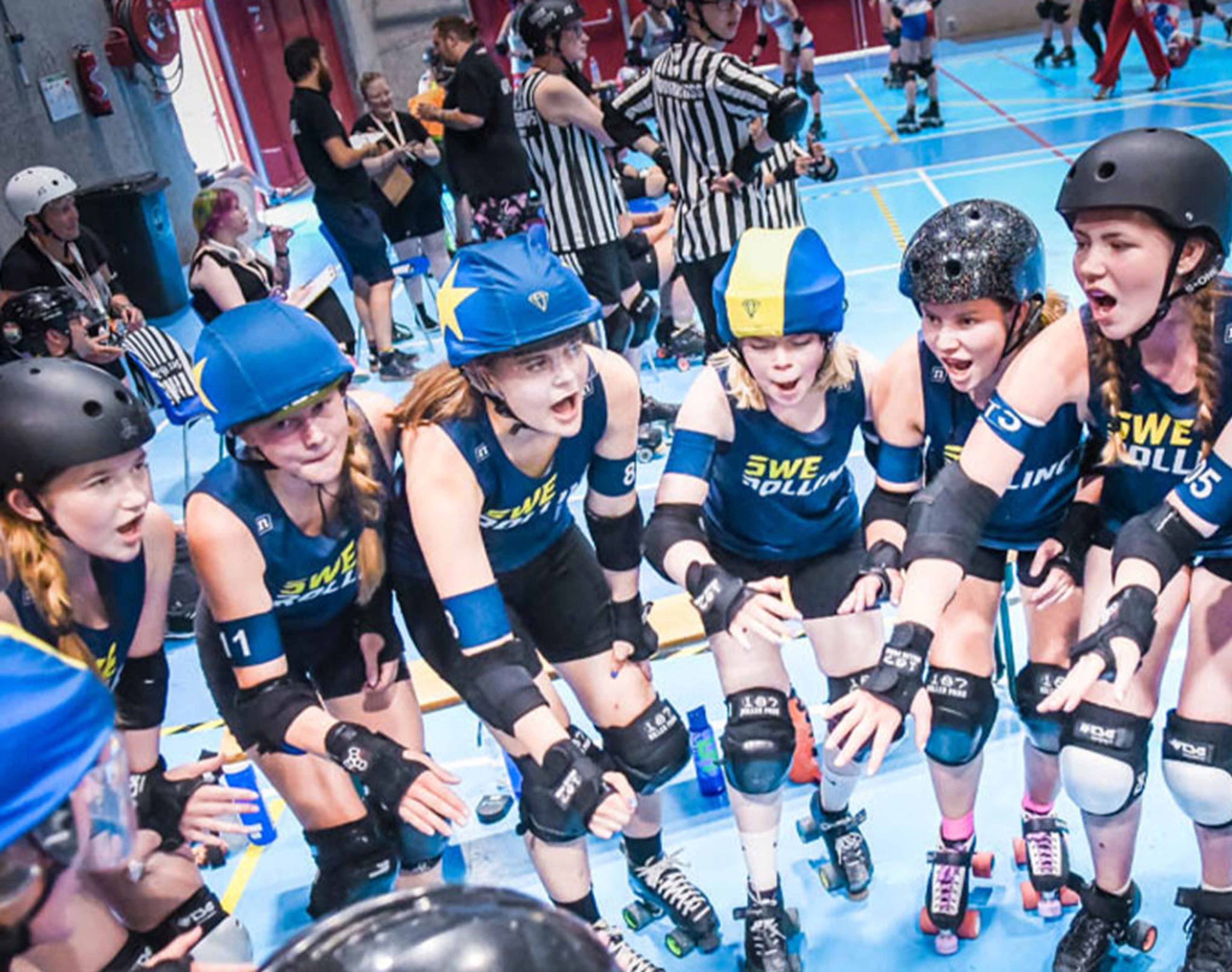 Juniorer i rullskridskor med blå och gula hjälmar samlade i en cirkel inför en match i roller derby. De bär skyddsutrustning och matchtröjor med texten "SWE".