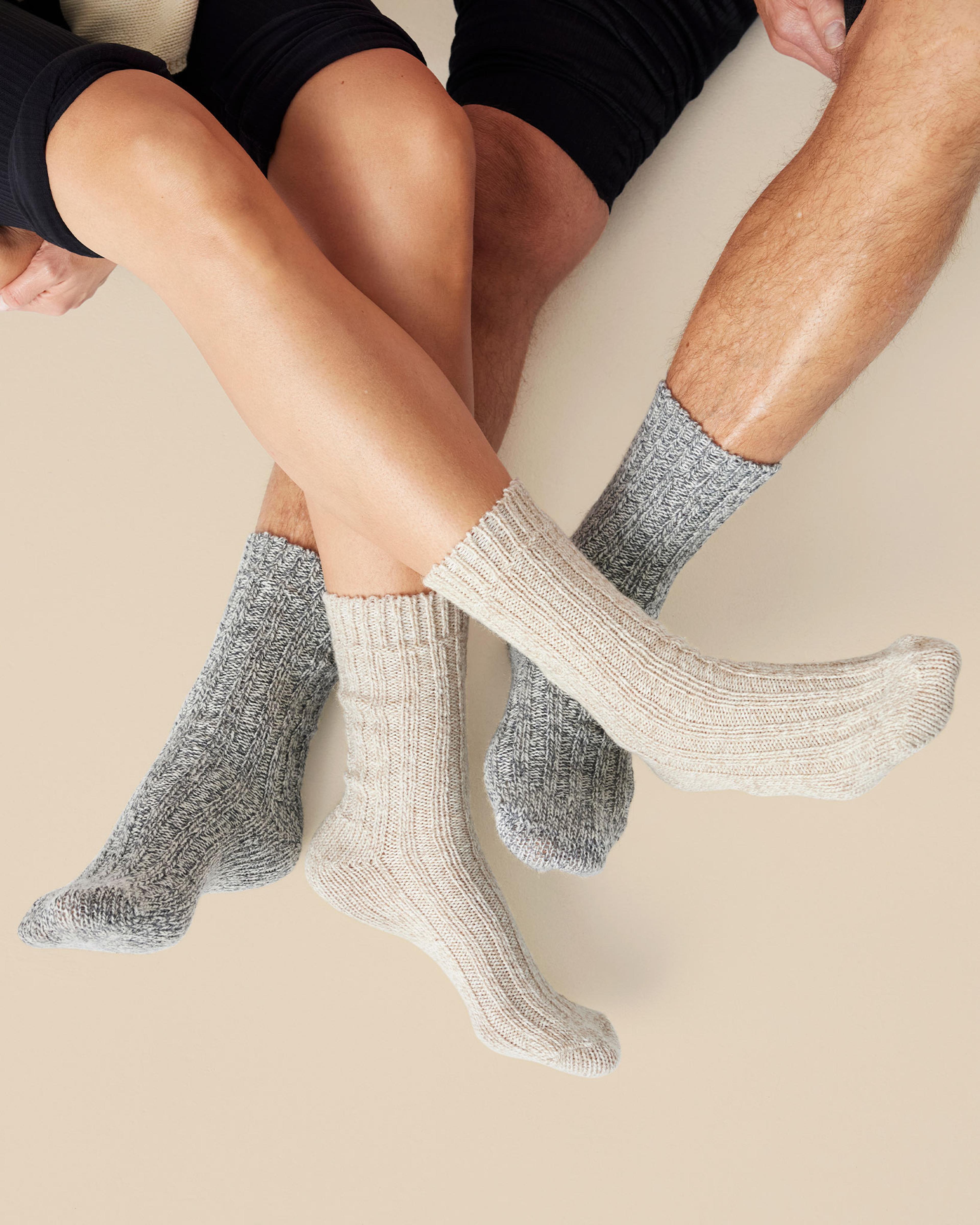 Två par tjocka, stickade raggsockor i mjuka nyanser av grått och beige. Sockorna har en ribbad struktur som ger både värme och komfort.