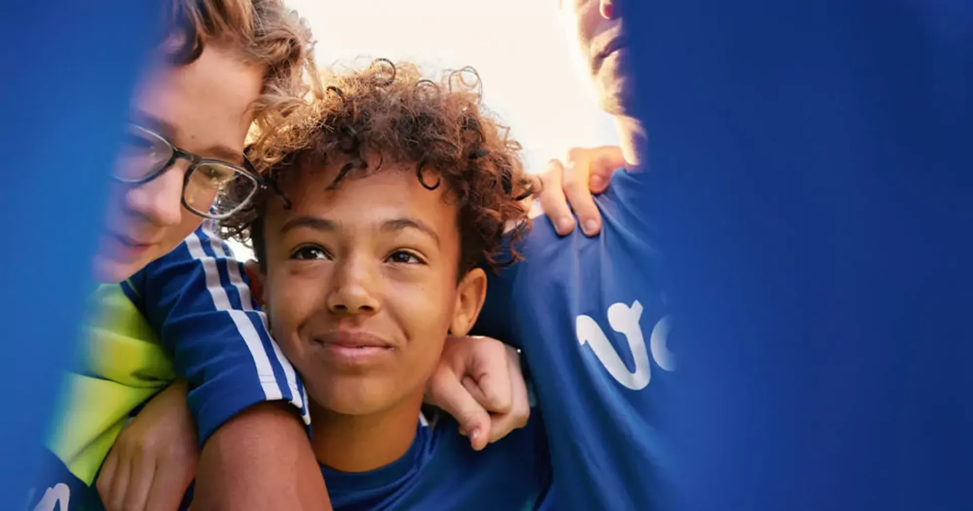 Tre personer i blå tröjor står tätt tillsammans med armarna om varandra. Deras ansikten syns delvis genom ett blått tyg.