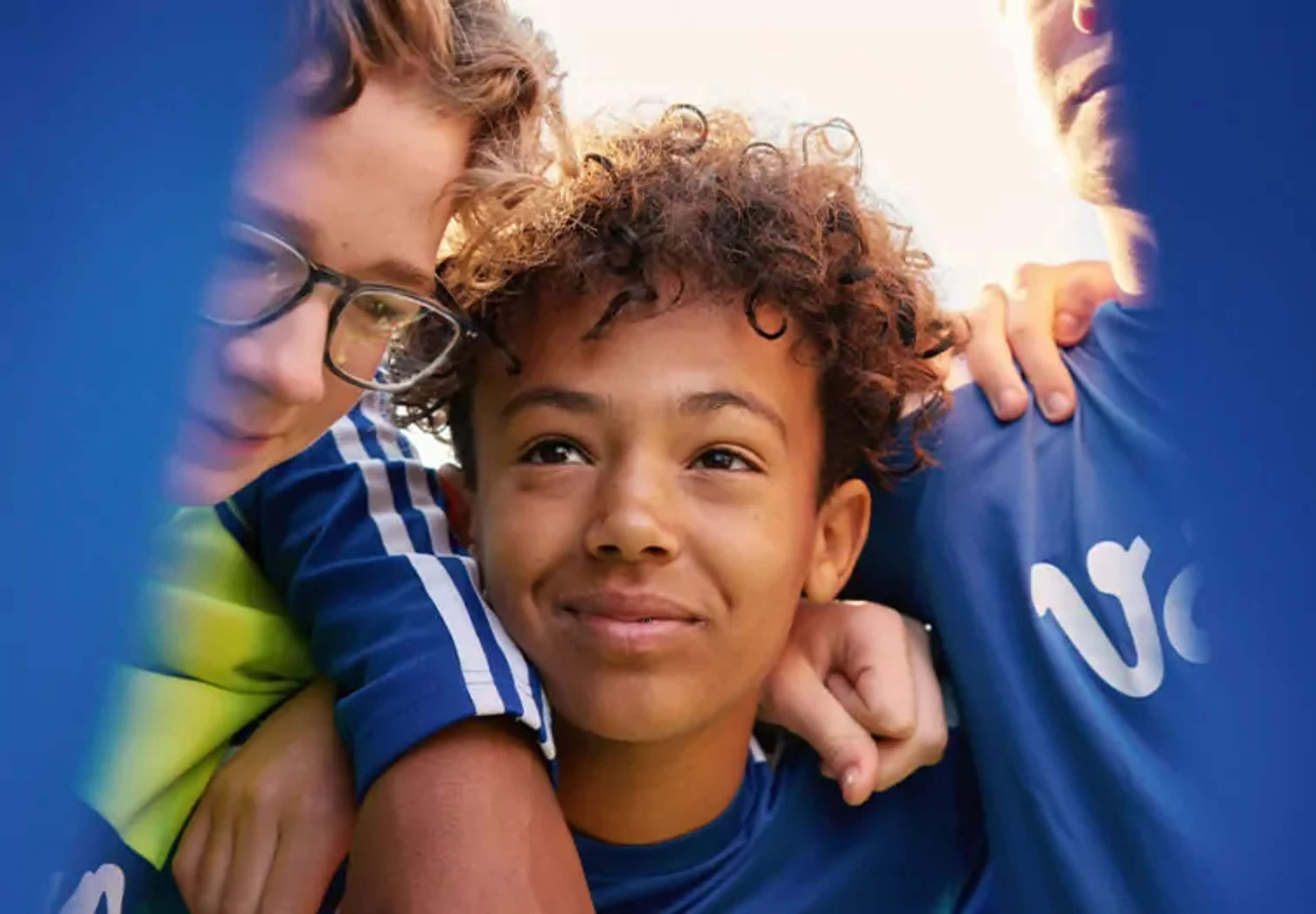 Tre personer i blå tröjor står tätt tillsammans med armarna om varandra. Deras ansikten syns delvis genom ett blått tyg.