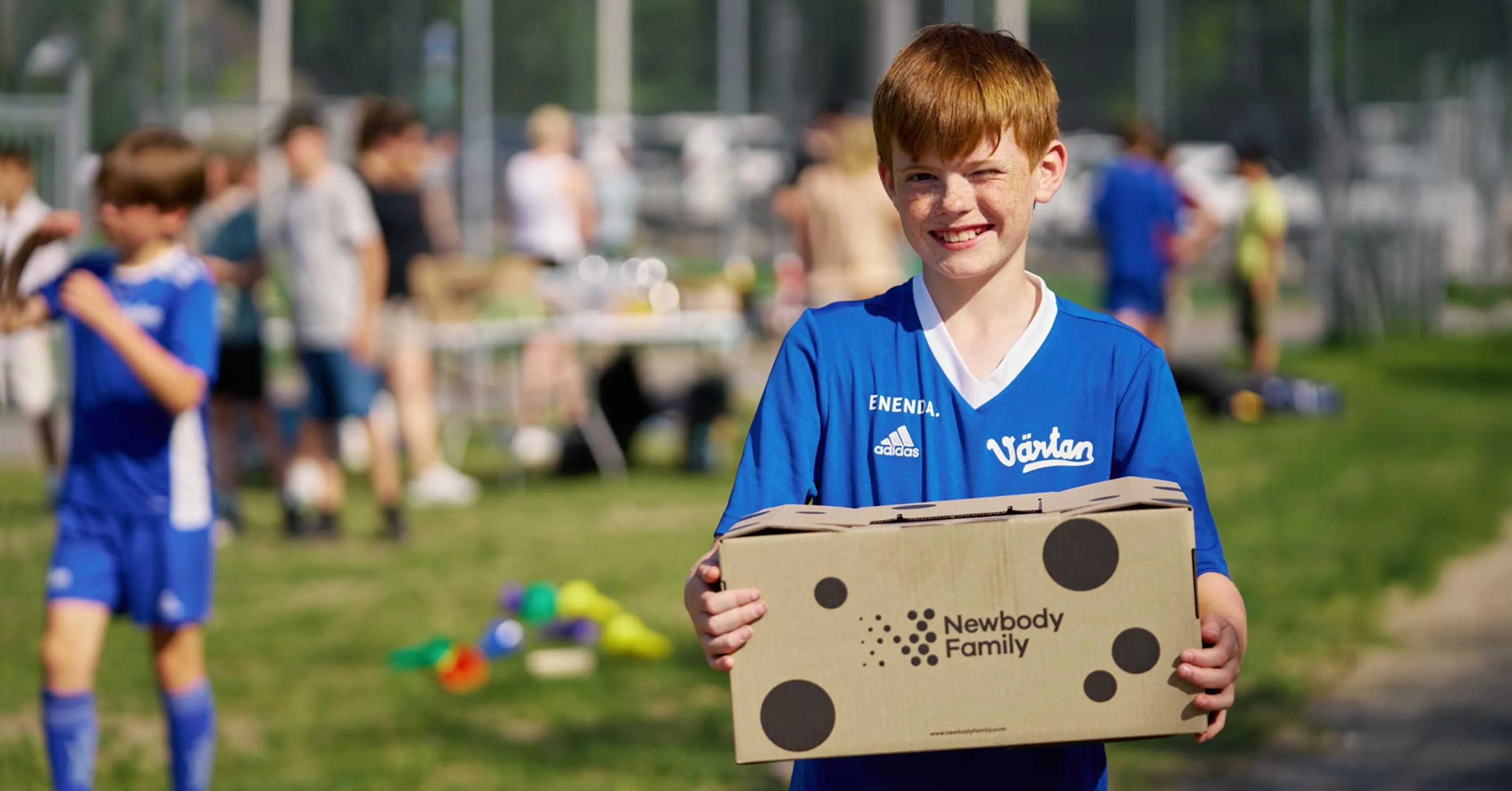 Fotbollkille på en fotbollsplan med en newbody kartong i famnen.