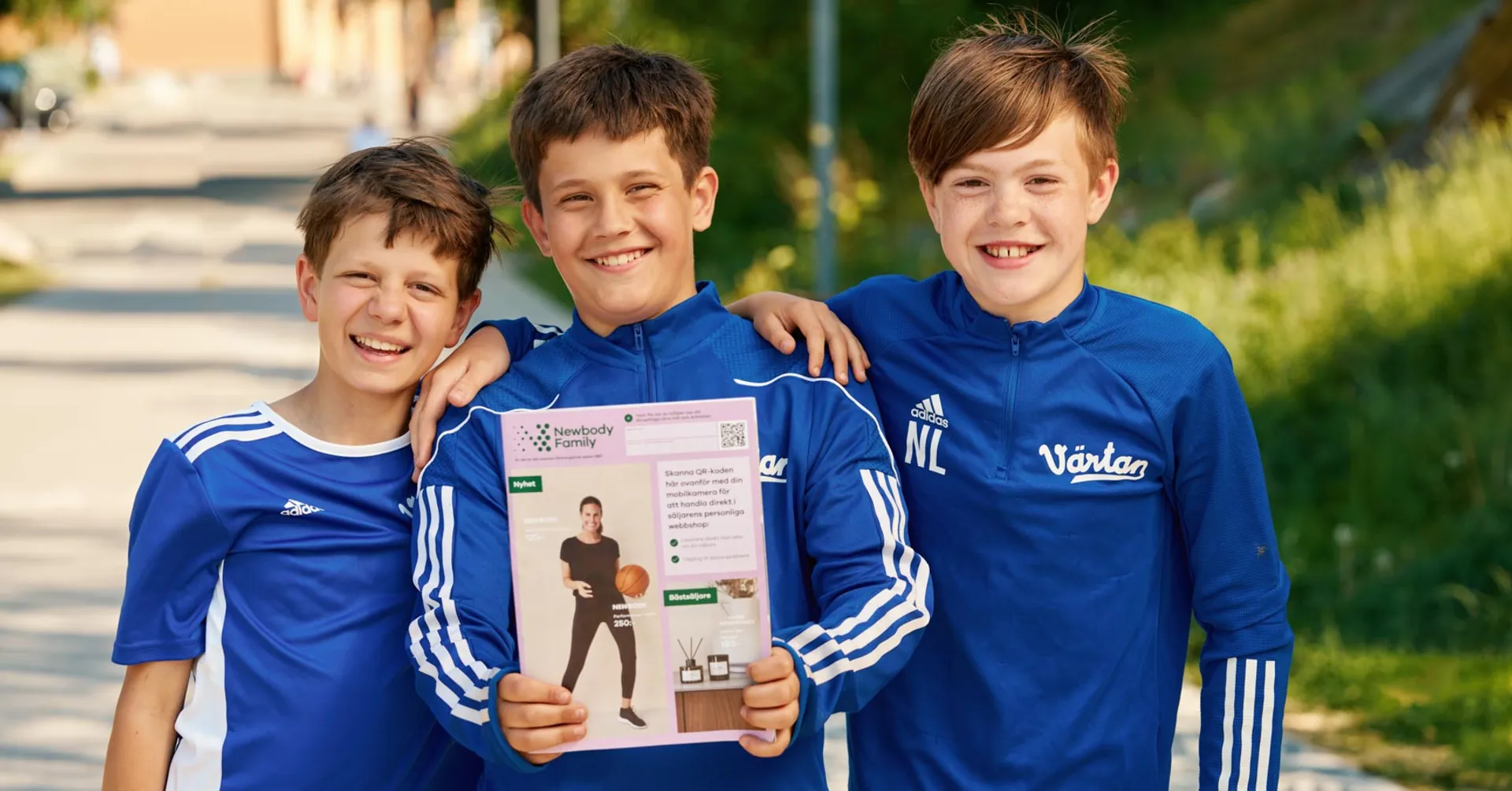 Tre fotbollskillar står bredvid en fotbollsplan, leendes med en Newbody katalog i famnen