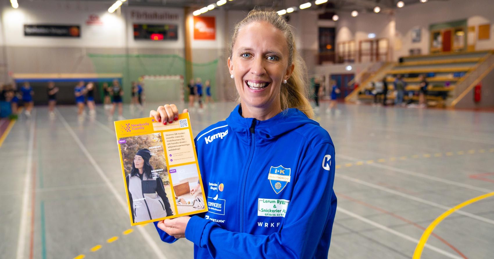 Kvinnlig handbollstränare iklädd träningskläder i en idrottshall, hållandes en Newbody katalog i handen.