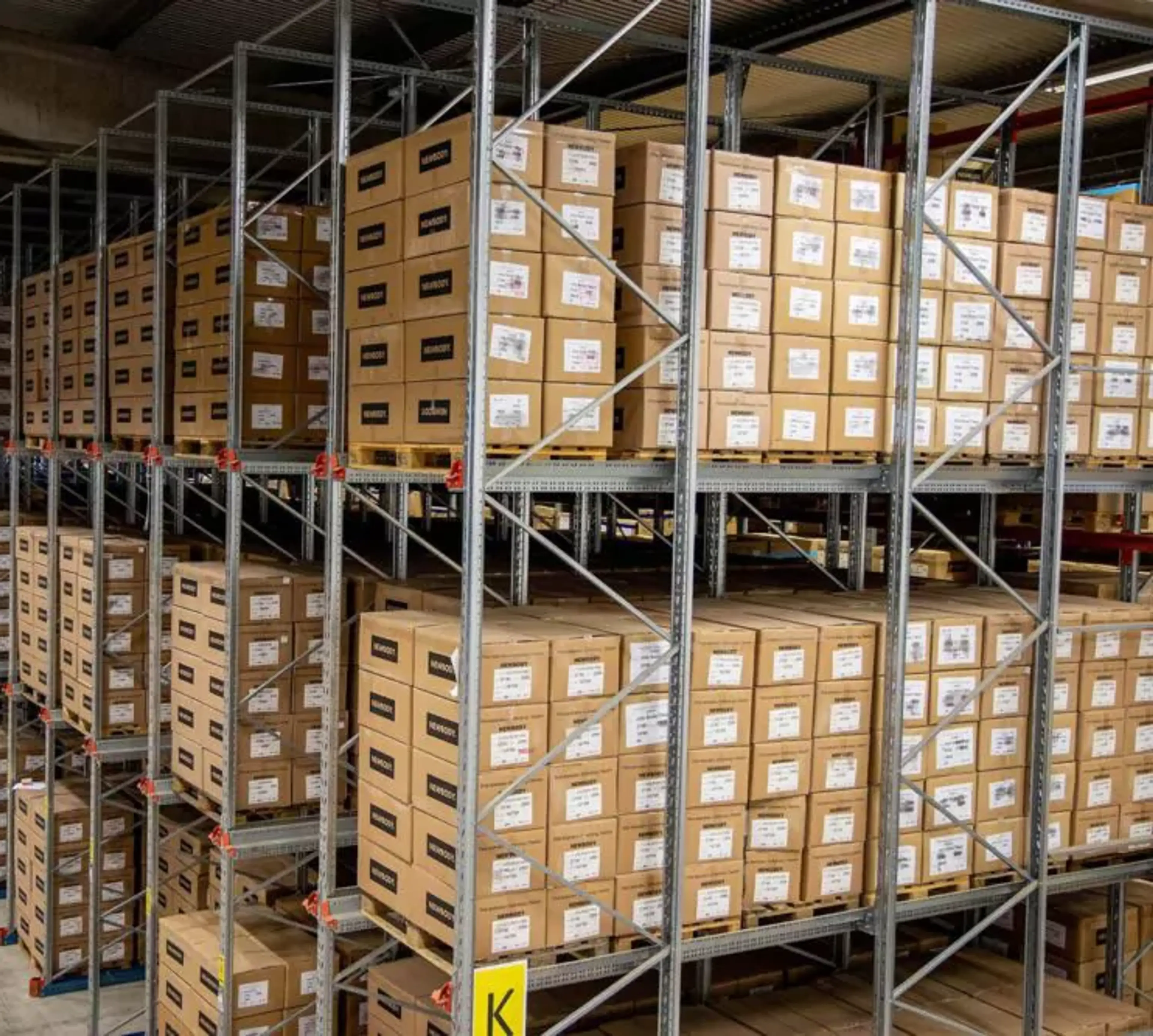Hyllor fyllda med prydligt staplade kartonger i ett stort lagerutrymme. En översikt av välorganiserad förvaring i en ljus och rymlig lokal.